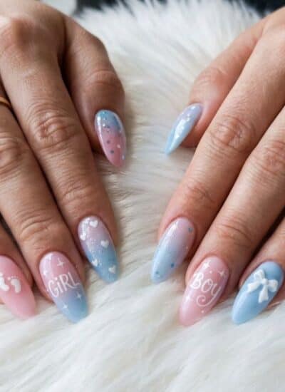 Two hands with manicured nails featuring blue and pink ombre designs, white bows, and the words “GIRL” and “BOY” written on the ring fingers.