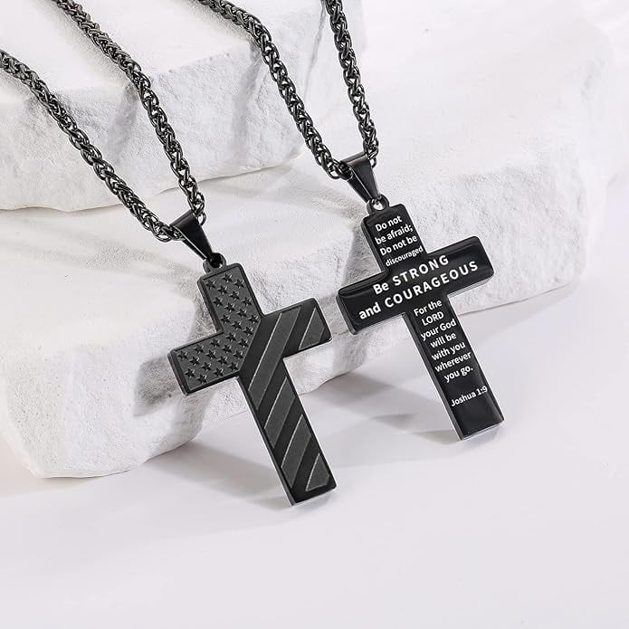 Two black cross necklaces on a white surface; one features a chevron and stars design, the other displays text from Joshua 1:9 about strength and courage.