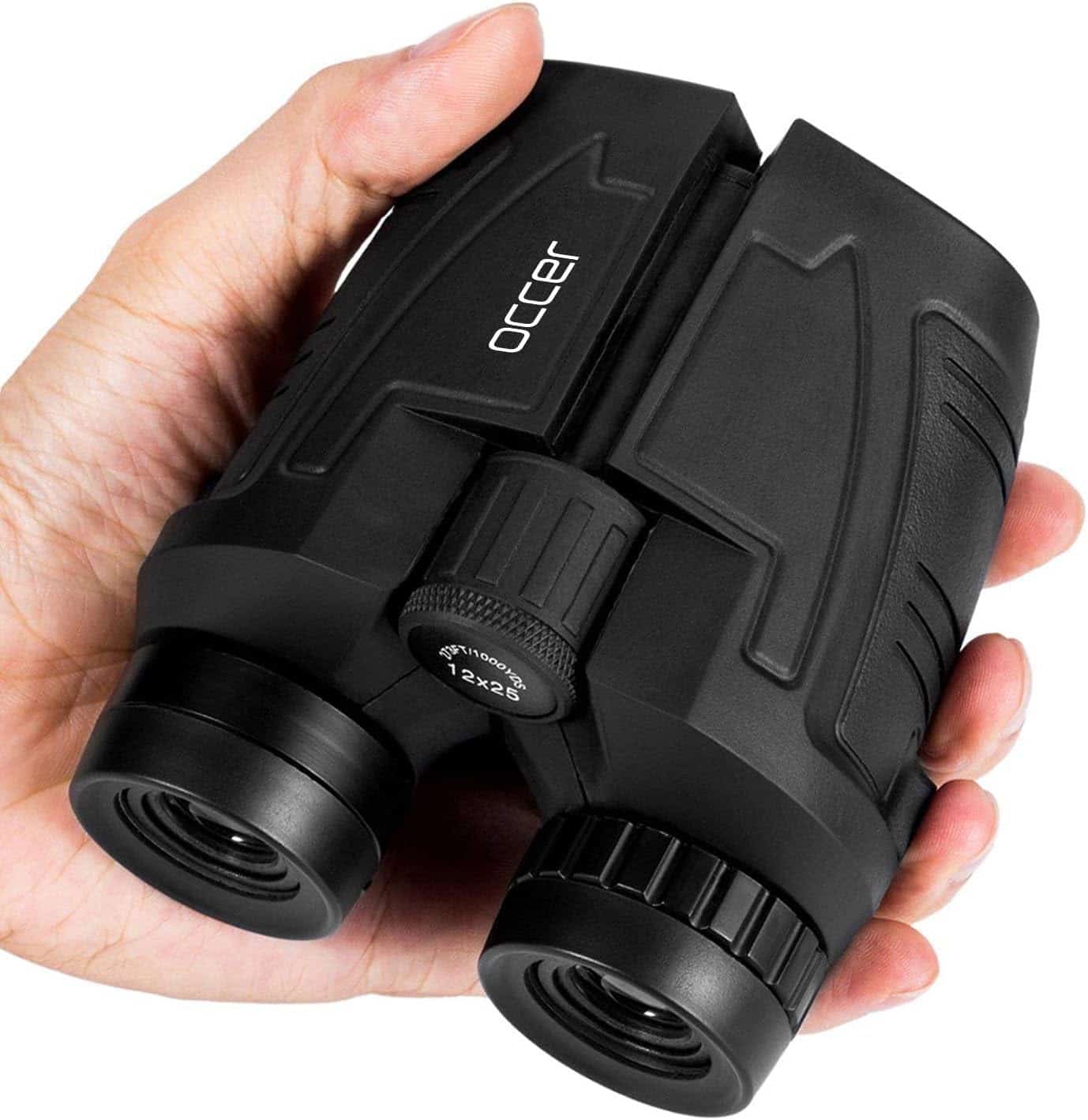 A hand holding a compact black pair of Occer brand binoculars, showing the eyepieces and central focus wheel.
