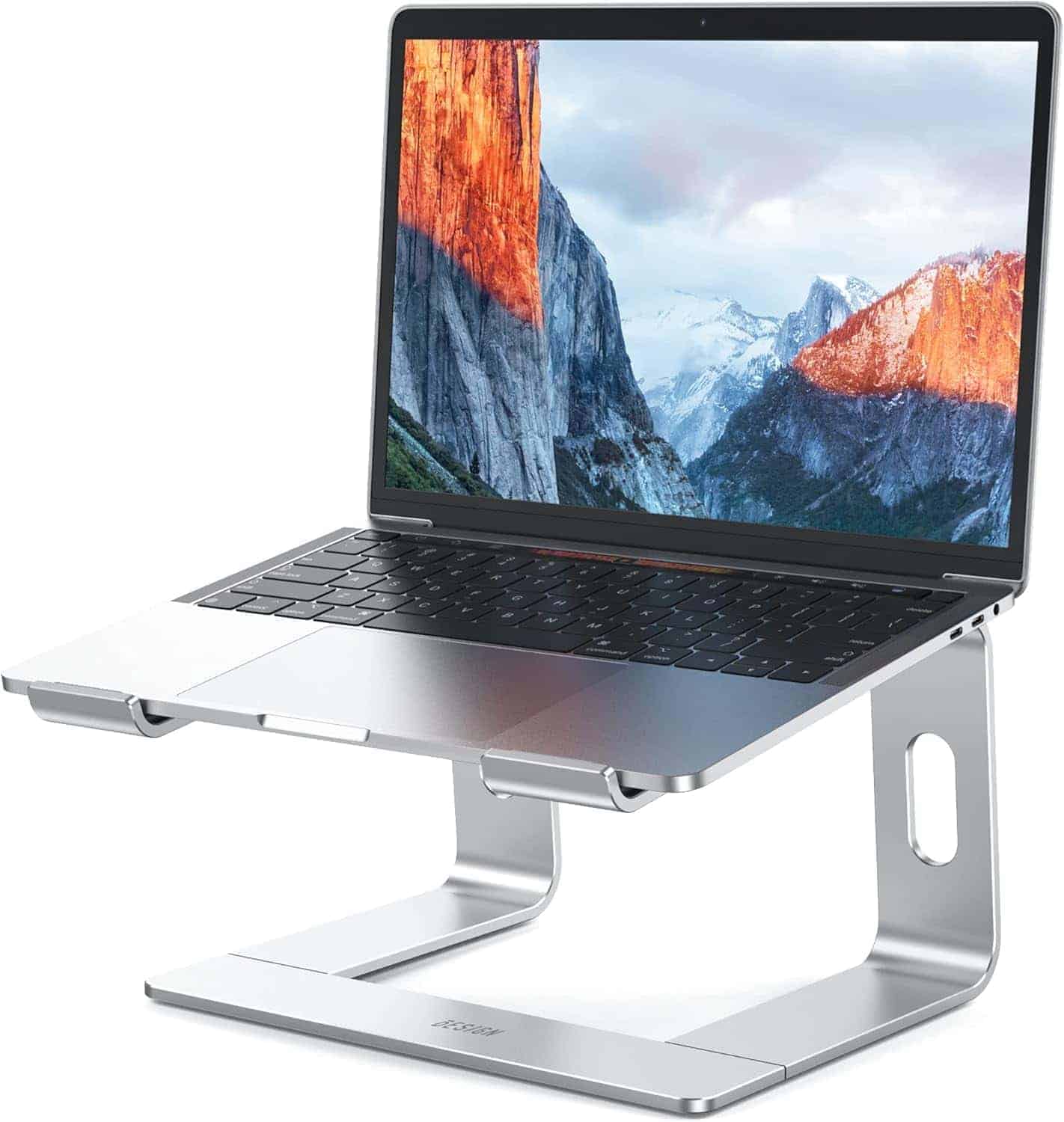 A silver laptop on a metallic stand, displaying a mountain landscape on its screen. The stand elevates the laptop above the surface.