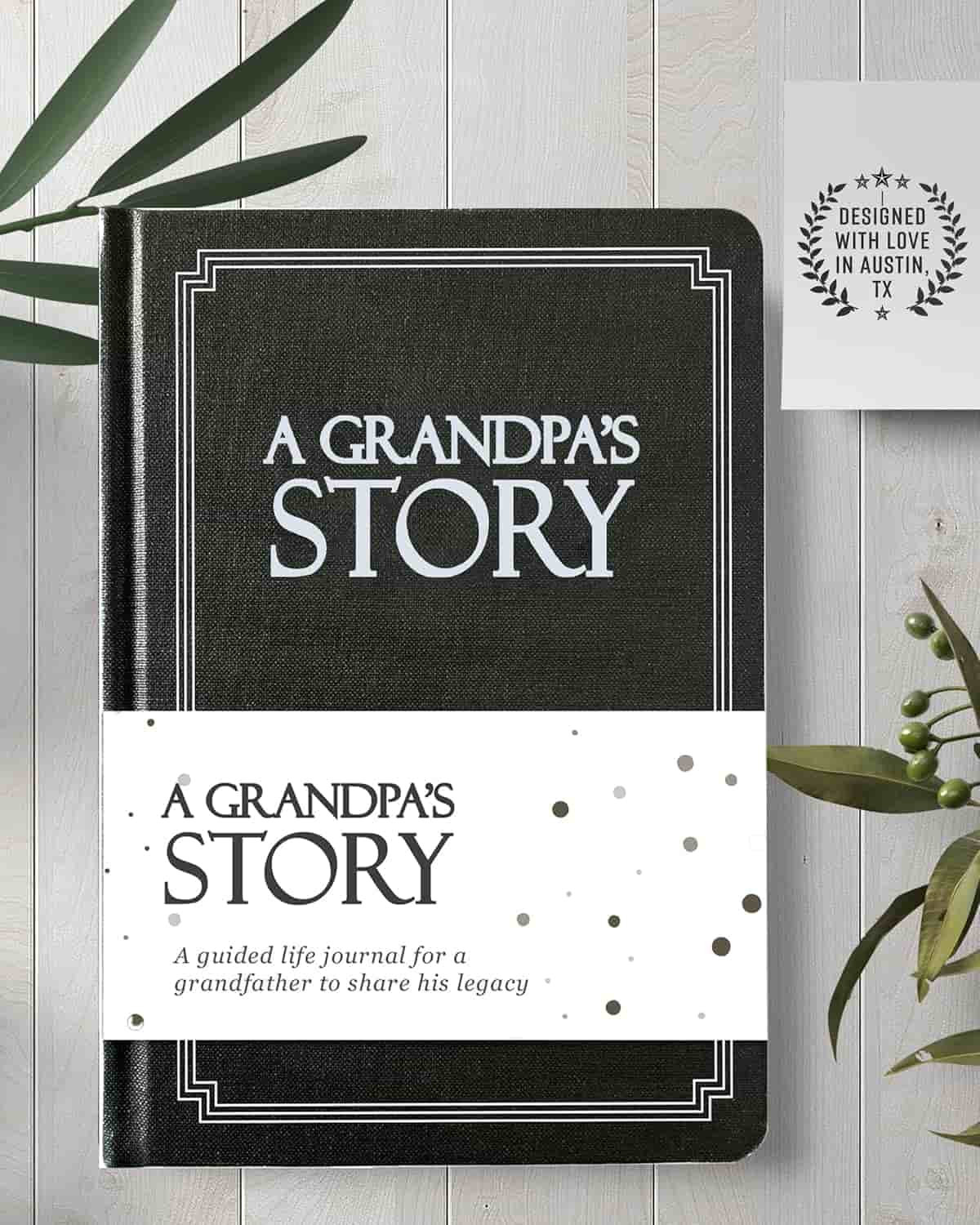 A black journal titled "A Grandpa’s Story" lies on a wooden surface with a white band that reads, "A guided life journal for a grandfather to share his legacy.