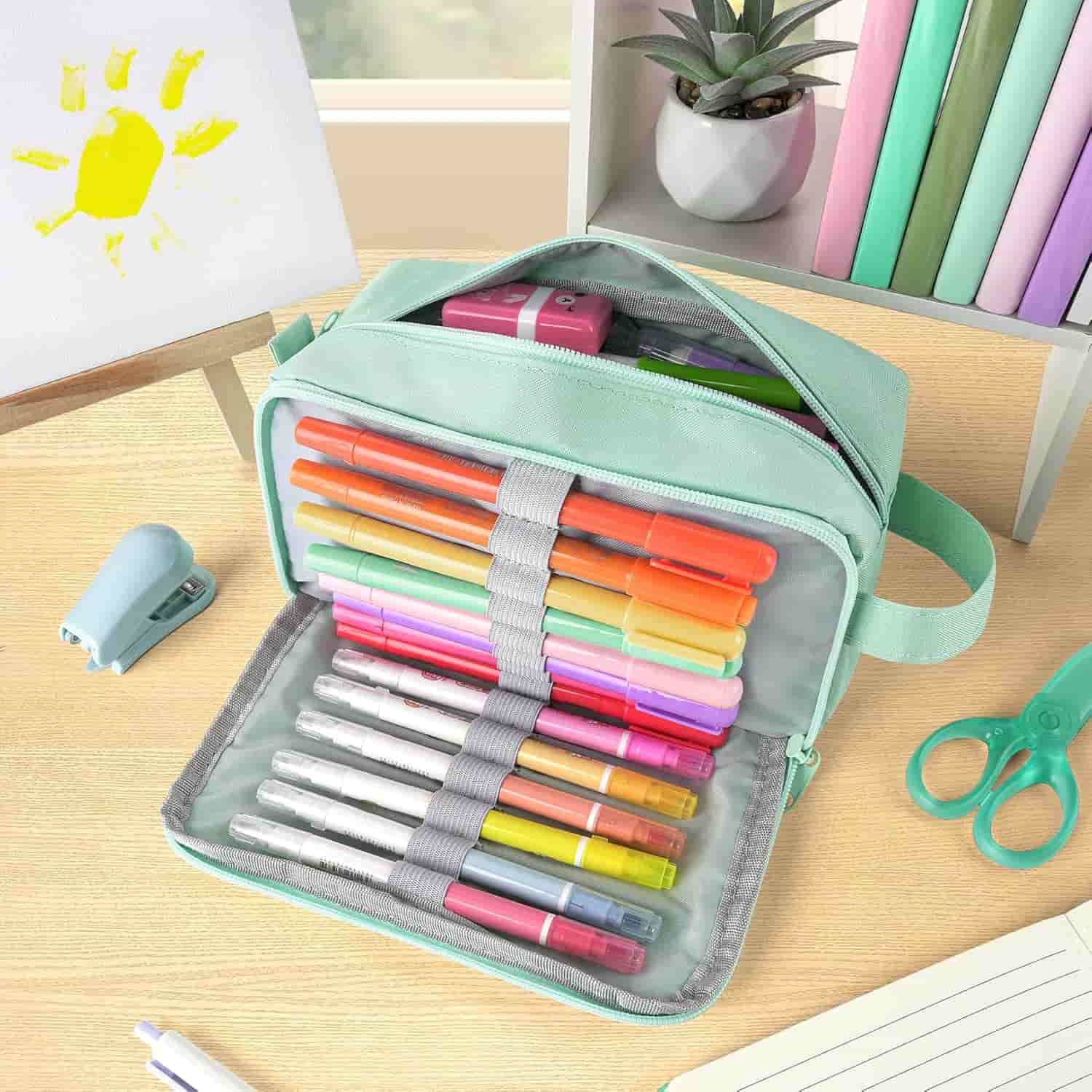 A mint green case with colorful markers organized inside, placed on a desk with scissors, a stapler, a plant, books, and a child's drawing of a sun.