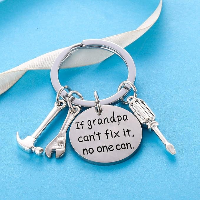A keychain with small tool charms and a round pendant engraved with "If grandpa can't fix it, no one can," on a blue background.