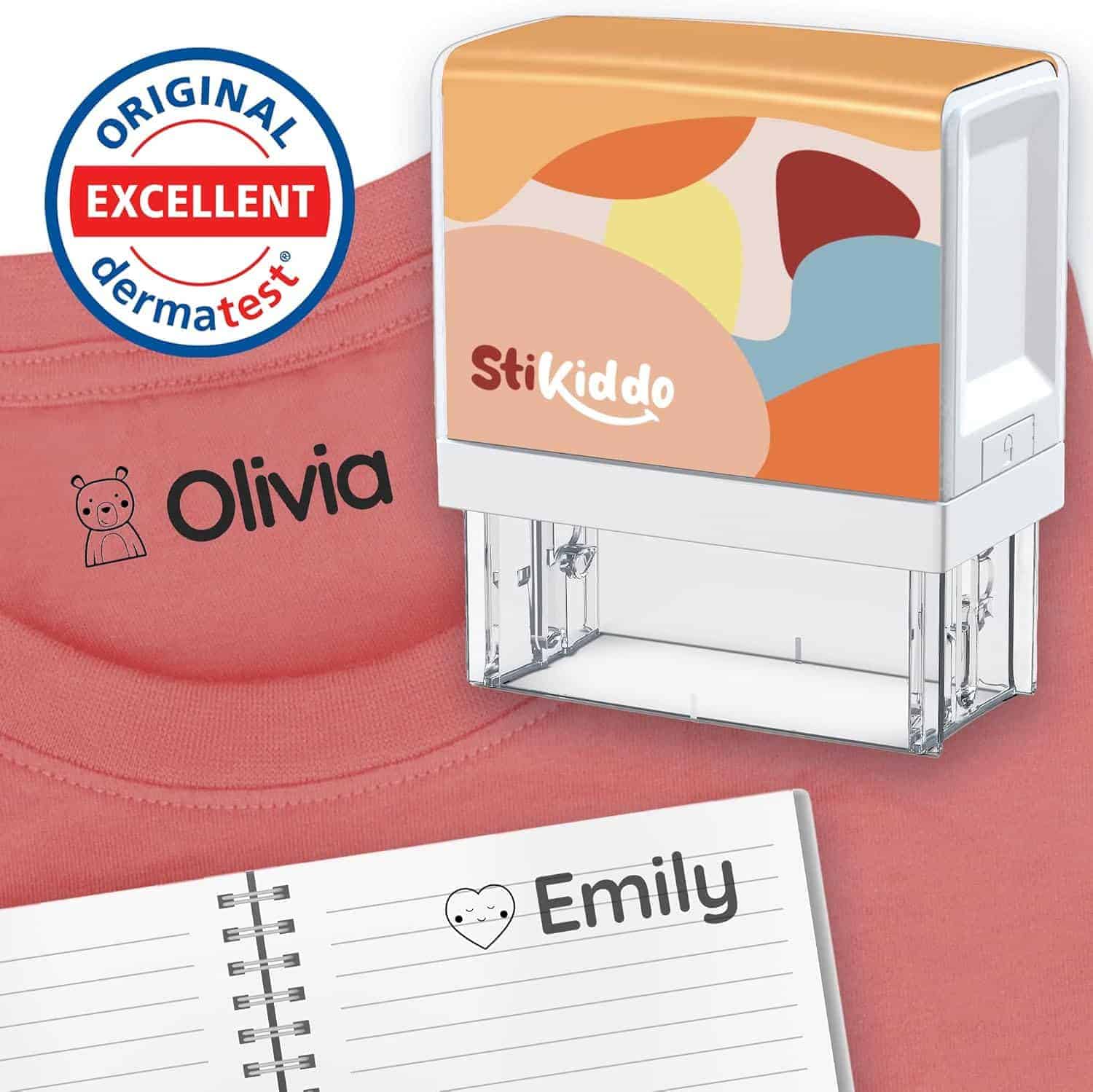 A personalized name stamp labeled "StiKiddo" is shown marking "Olivia" on a shirt and "Emily" in a notebook, with a Dermatest "excellent" seal visible.