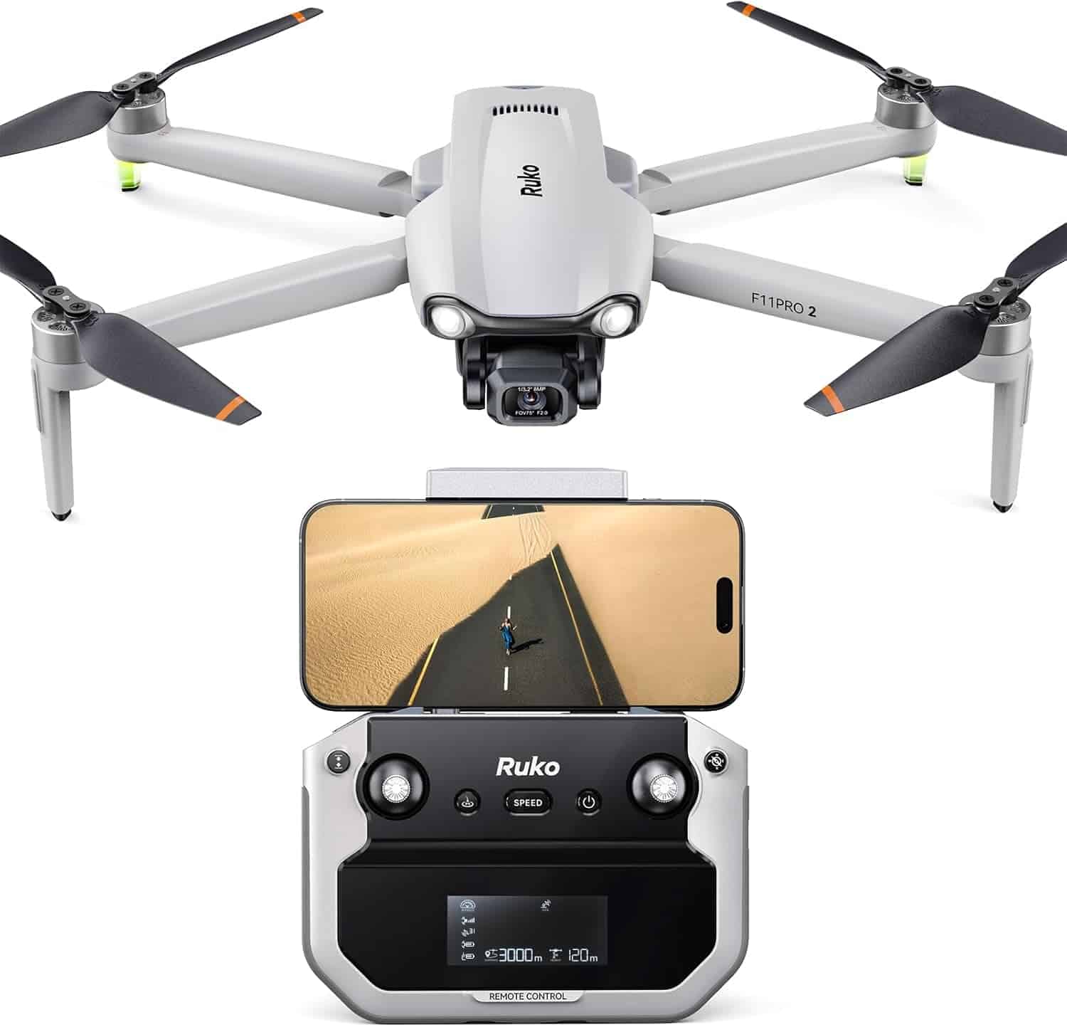 A white Ruko F11 GIM2 drone with camera is shown above a remote controller holding a smartphone displaying an aerial view of a road in a desert.
