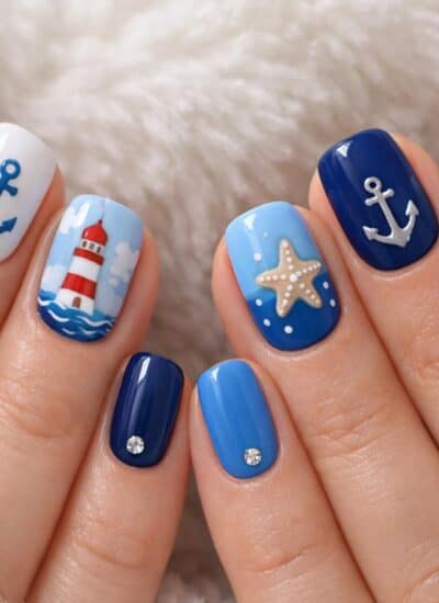Hands with blue and white nautical-themed nail art, featuring anchors, starfish, a lighthouse, birds, and small decorative gems.