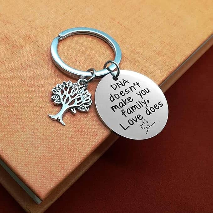 A keychain with a tree charm and a round metal tag engraved with the words, "DNA doesn't make you family. Love does," resting on a closed book.