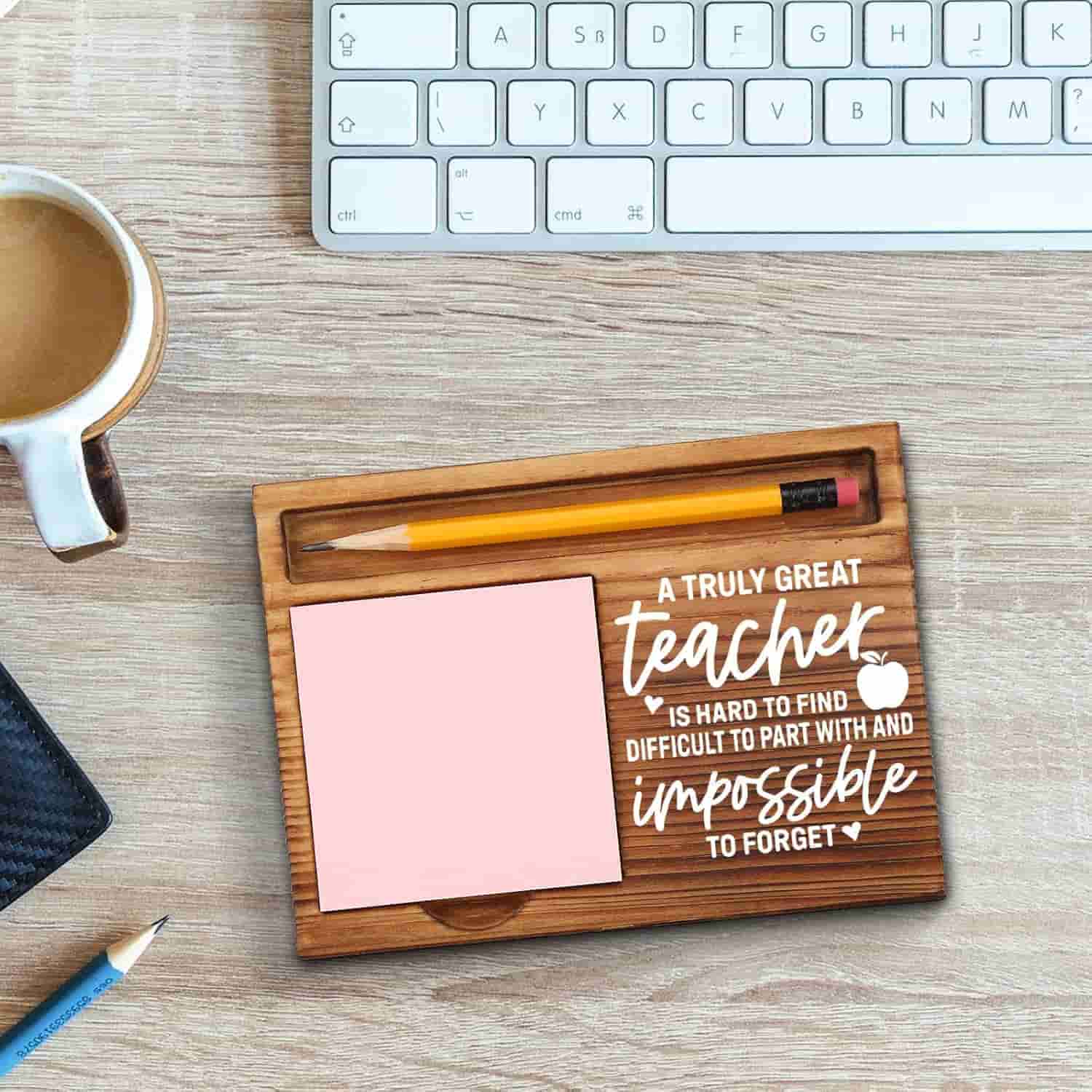 A wooden desk organizer with a pencil, pink sticky notes, and the words "A truly great teacher is hard to find, difficult to part with, and impossible to forget.
