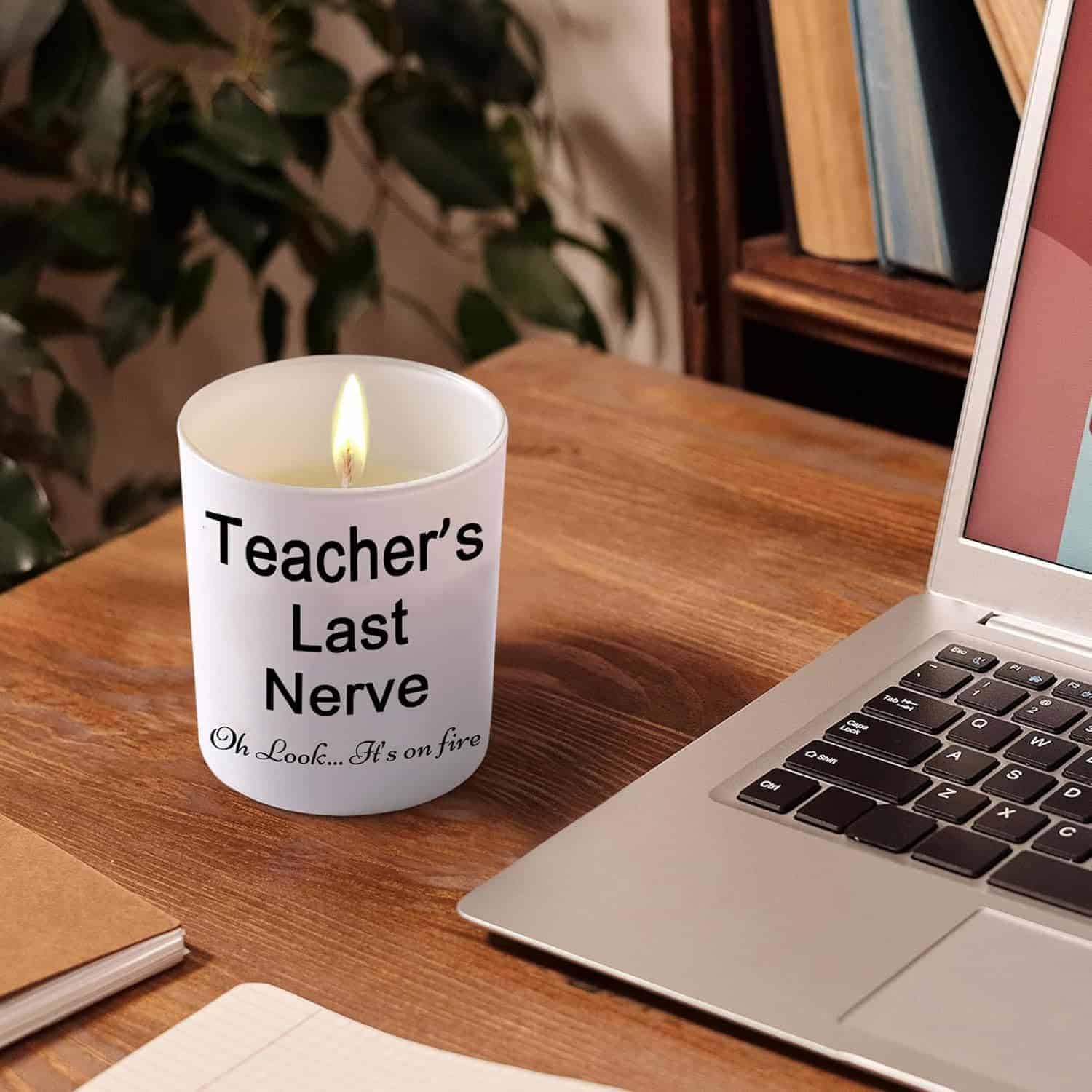 A lit candle on a wooden desk next to a laptop, labeled "Teacher's Last Nerve. Oh Look... It's on fire.