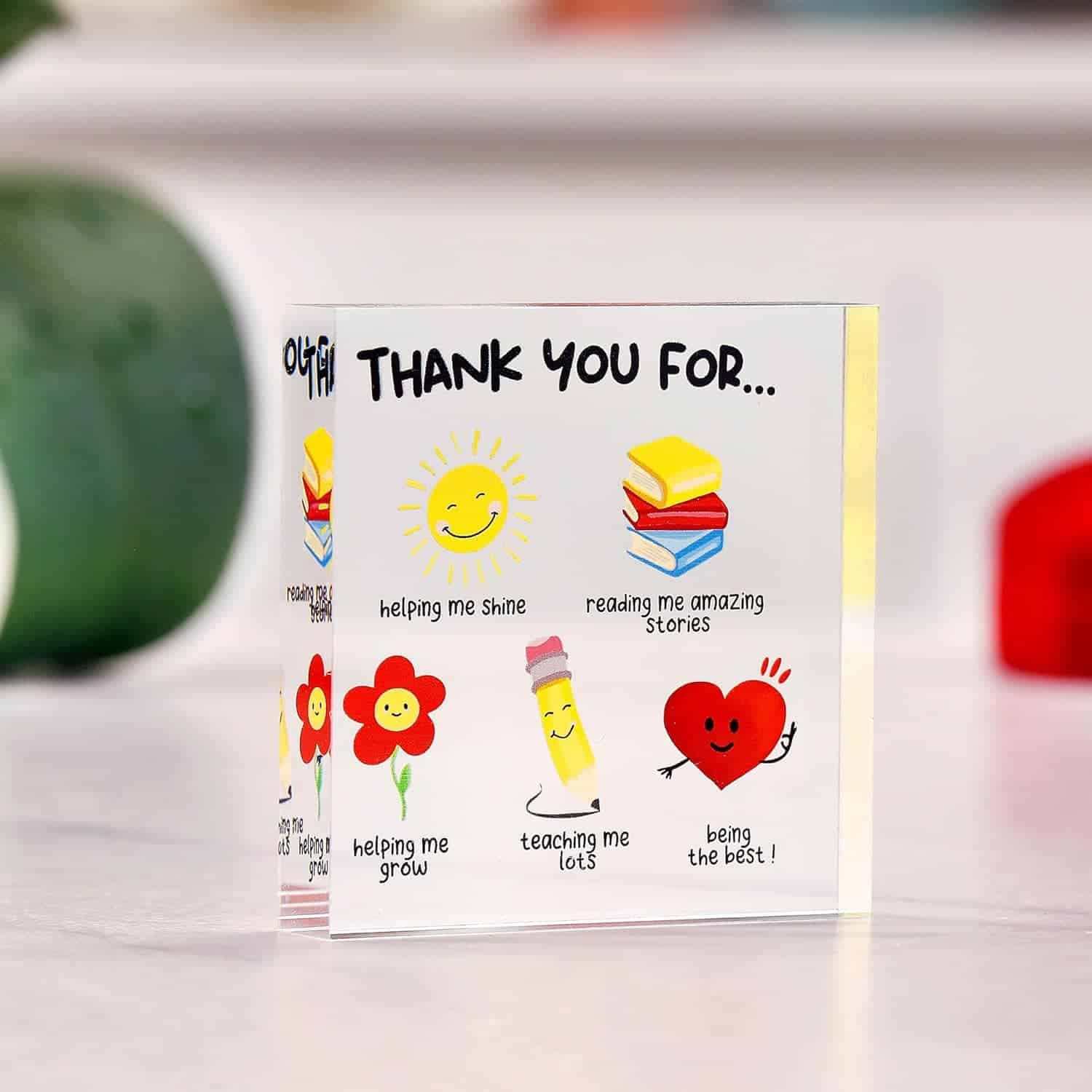 A small acrylic plaque with cartoon images and text thanking someone for helping, teaching, reading stories, and being supportive, placed on a table with blurred background.