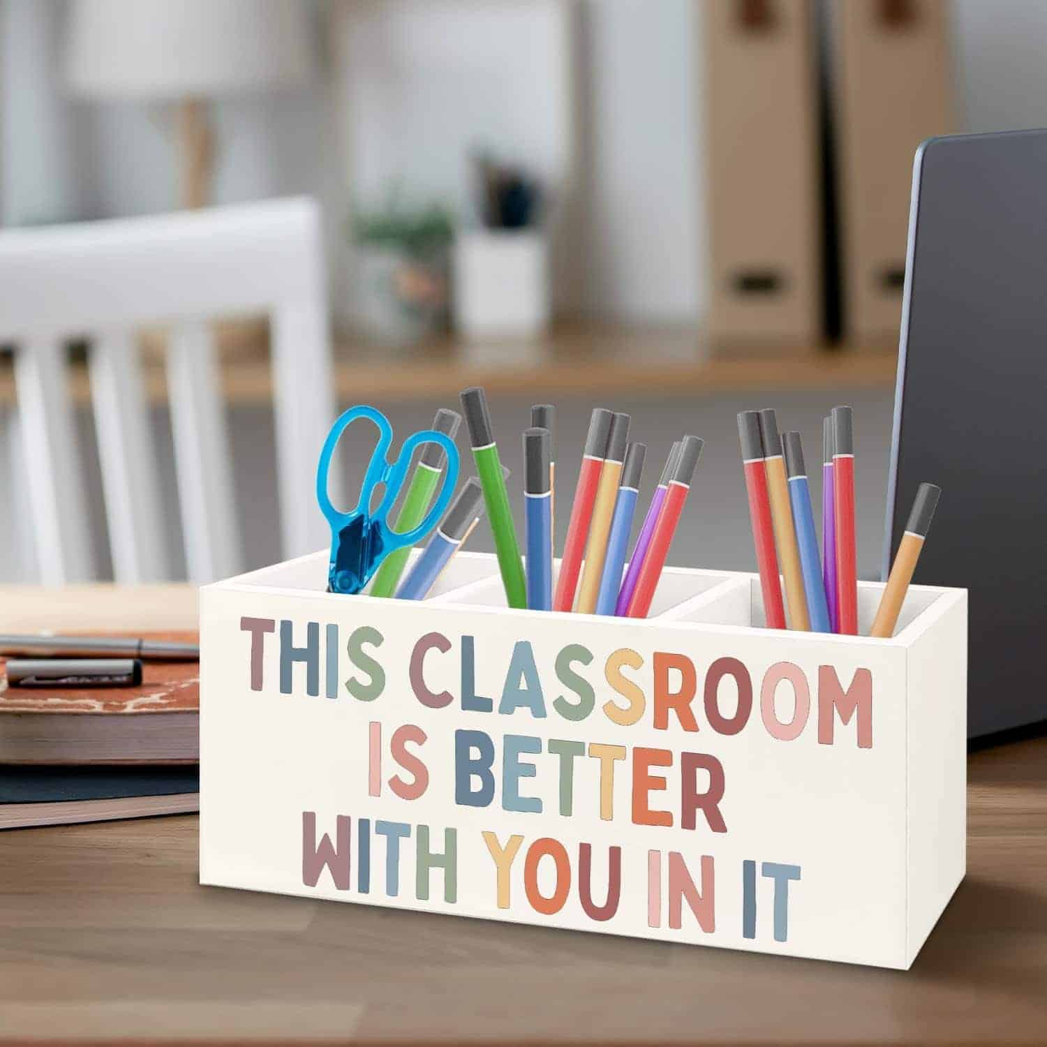 A desk organizer holding pens, pencils, scissors, and markers, with text reading, “This classroom is better with you in it.”.