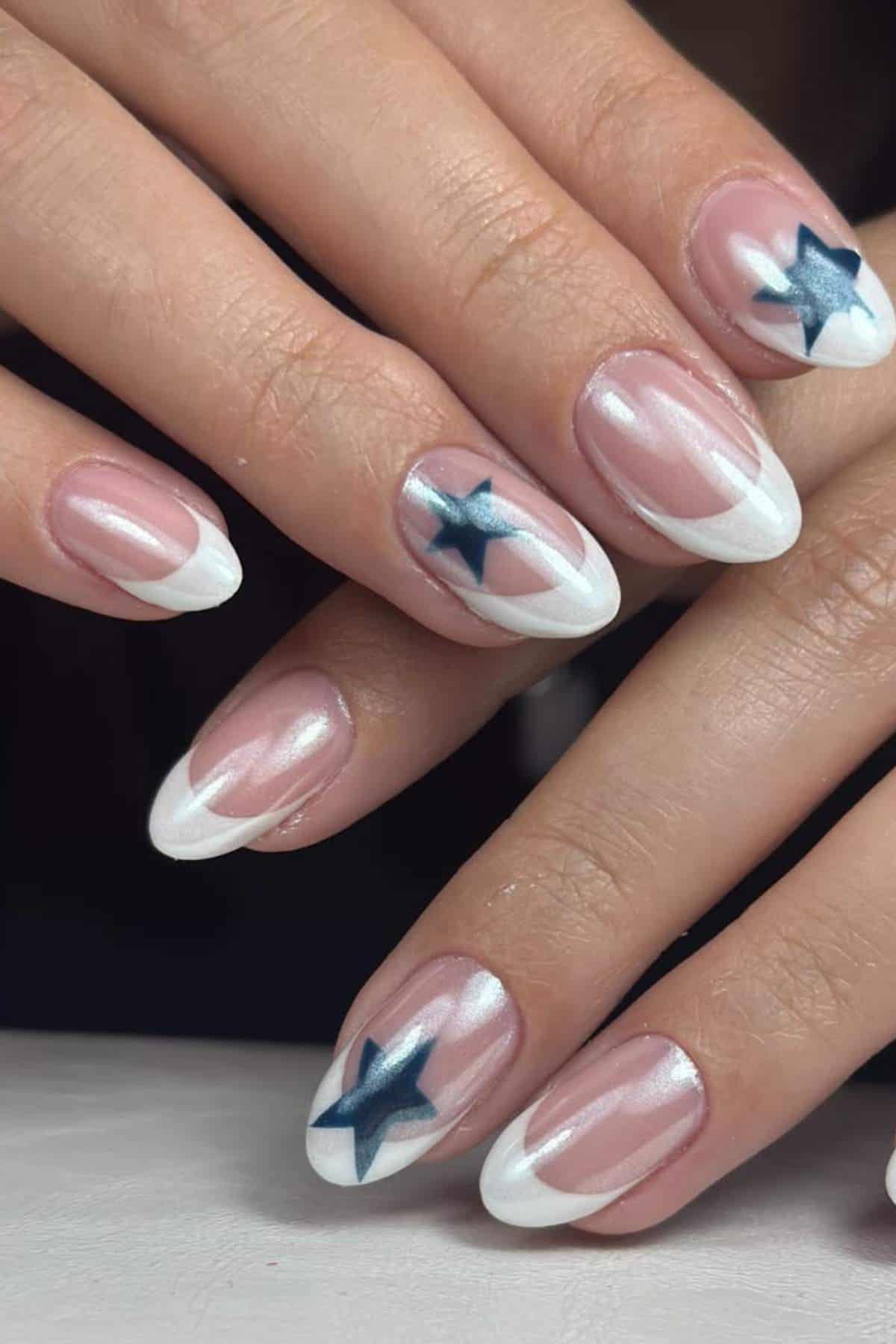 Close-up of hands with almond-shaped nails featuring white French tips and dark blue star designs on a clear base.