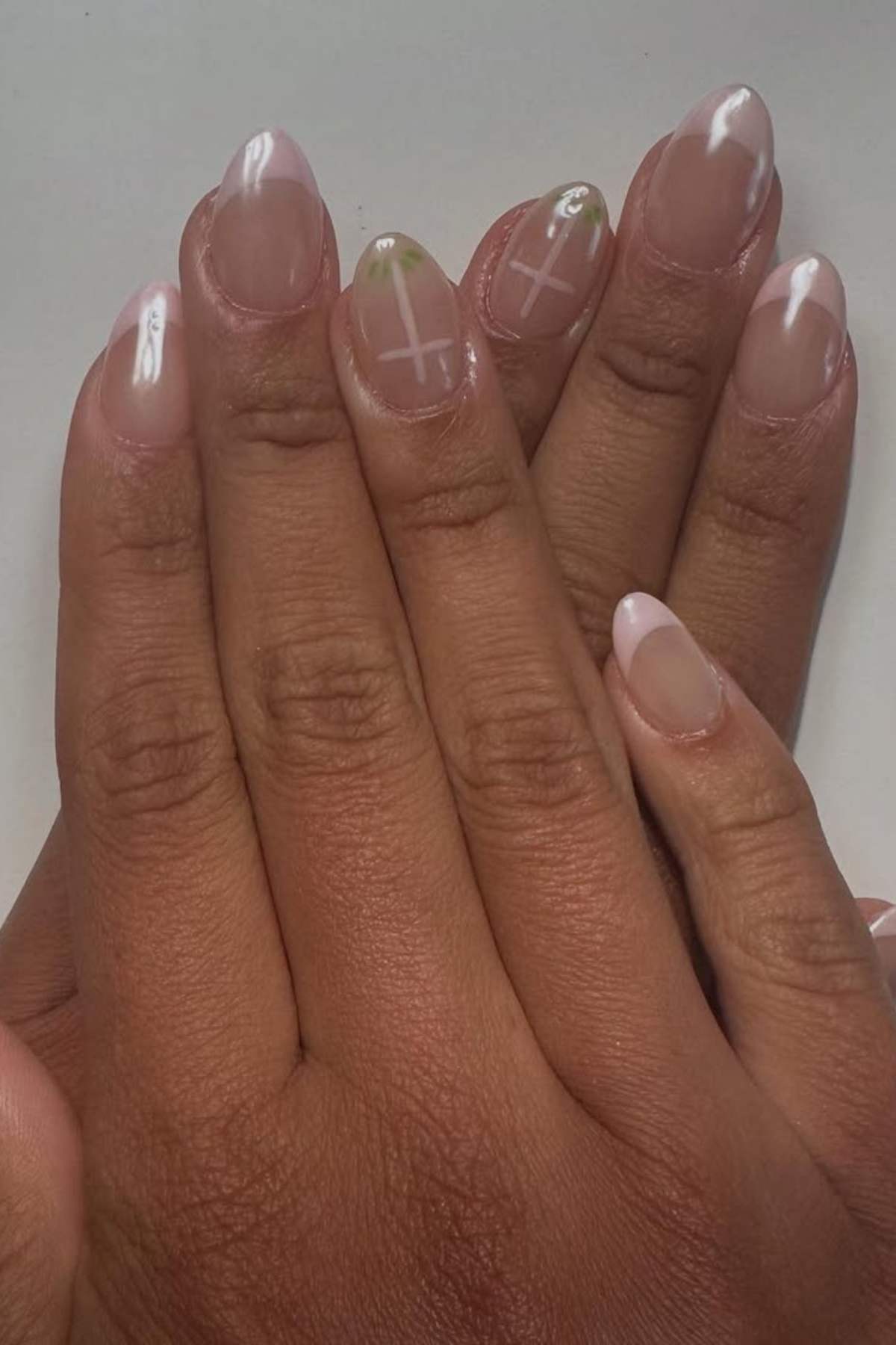A person with neatly manicured hands featuring nude nails with white tips and subtle cross designs on some nails.