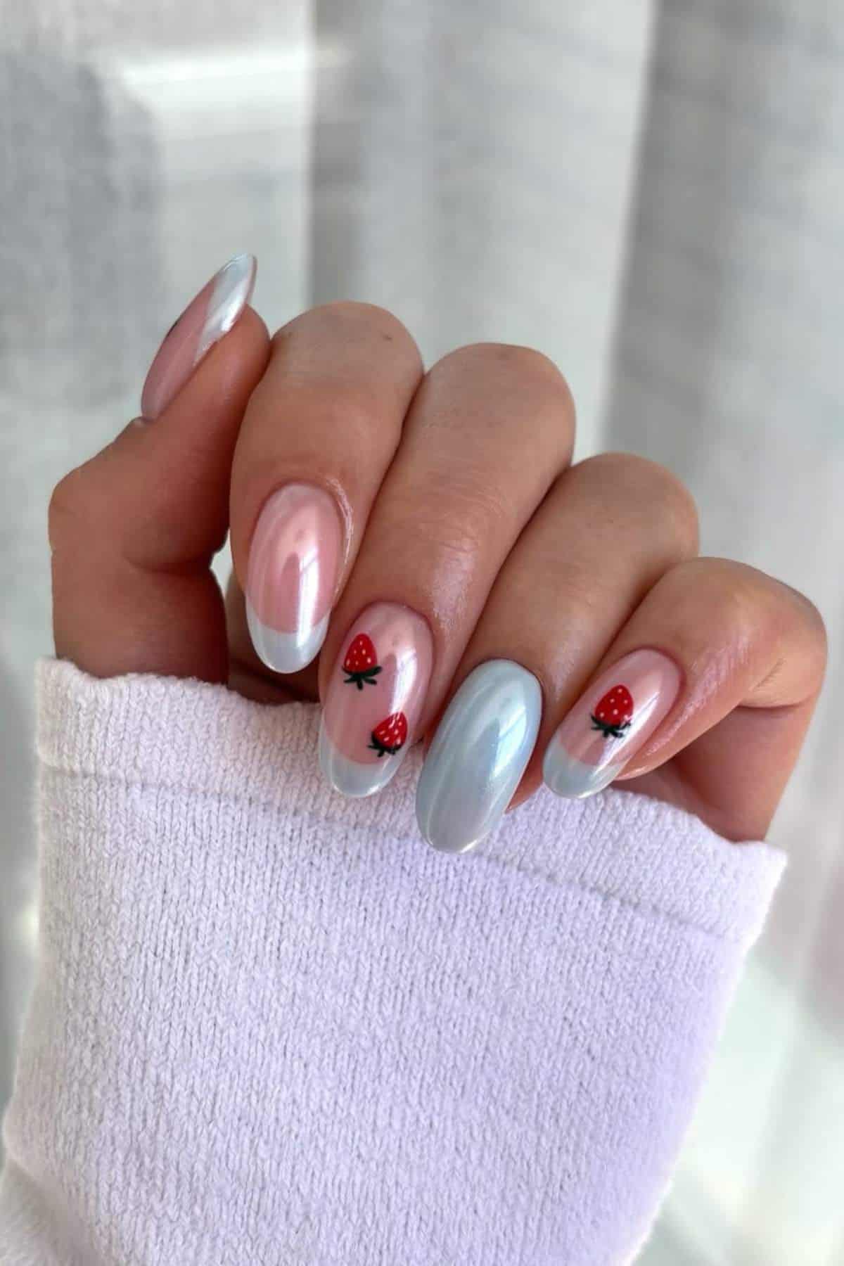 A hand with glossy pastel pink and light blue nails, two nails feature small ladybug designs, and the person is wearing a white long-sleeve top.