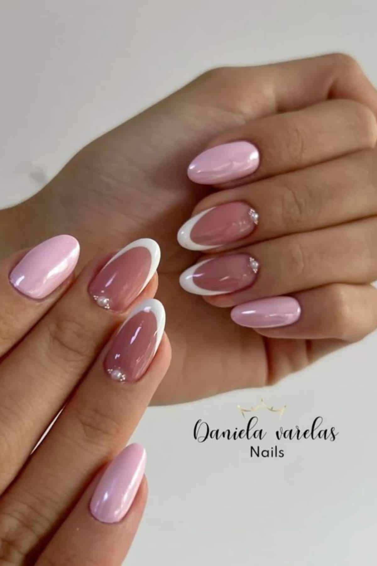 A hand displays manicured nails with pink polish, white tips, and small rhinestone accents. The nails are almond-shaped and glossy. The text reads "Daniela varelas Nails.