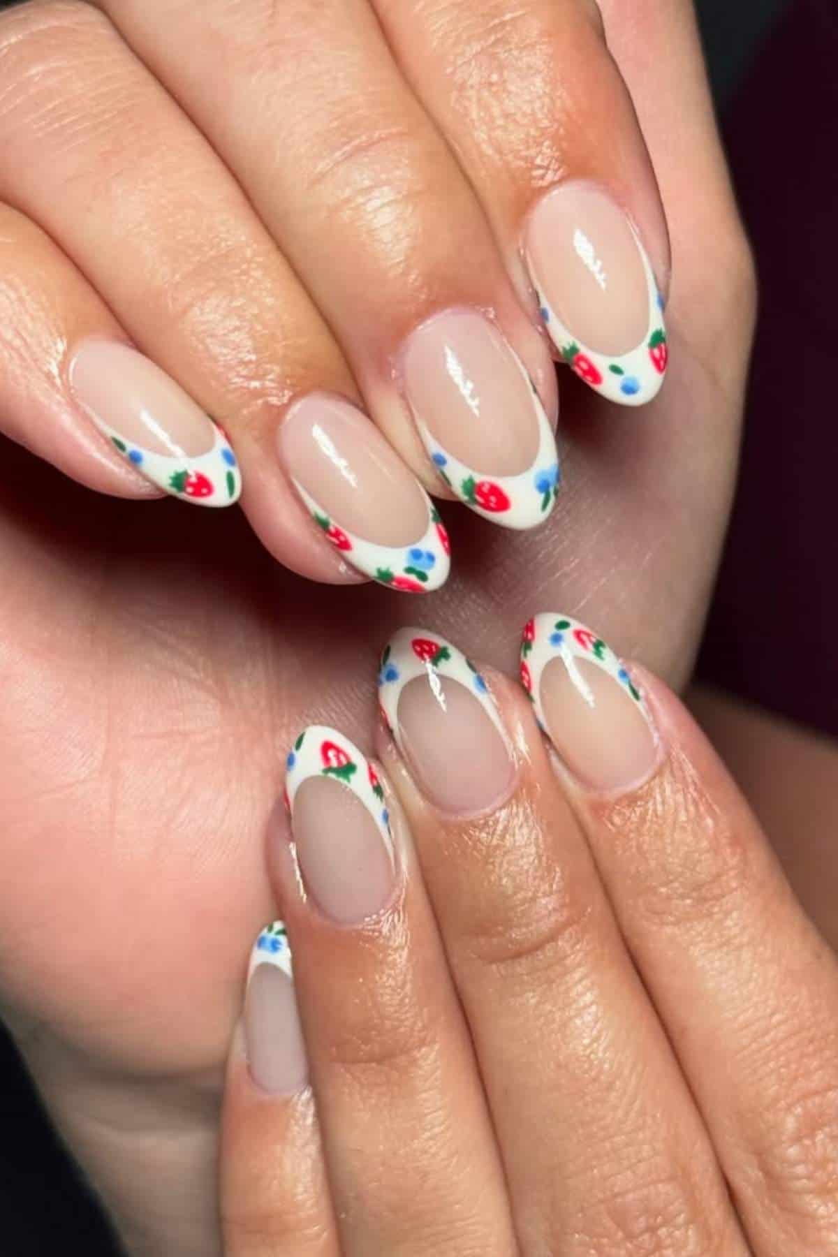 Hands with almond-shaped nails featuring a French tip design with small red, blue, and green floral patterns on each tip.