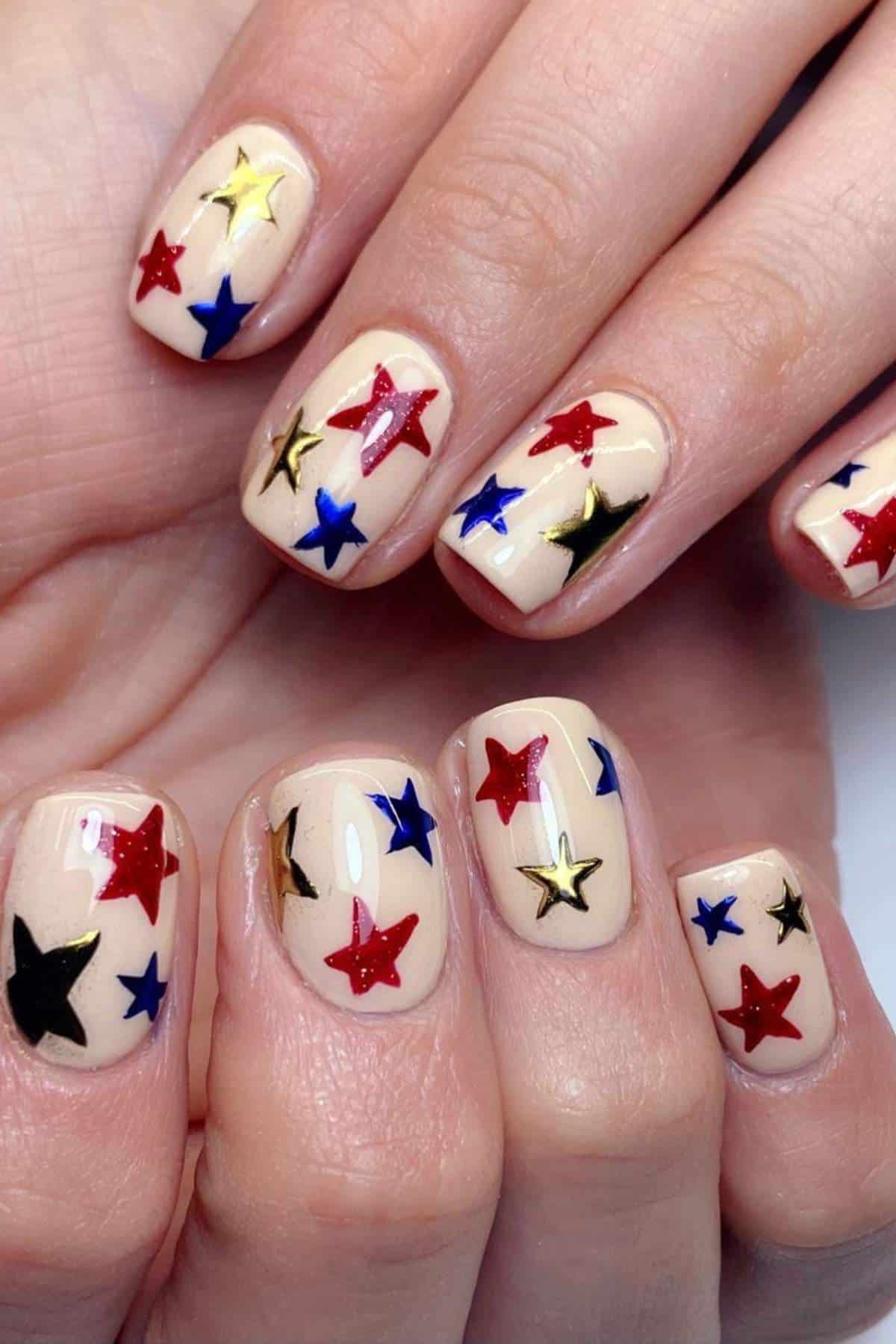 Fingernails painted with a nude base and decorated with red, blue, gold, and black star-shaped designs.