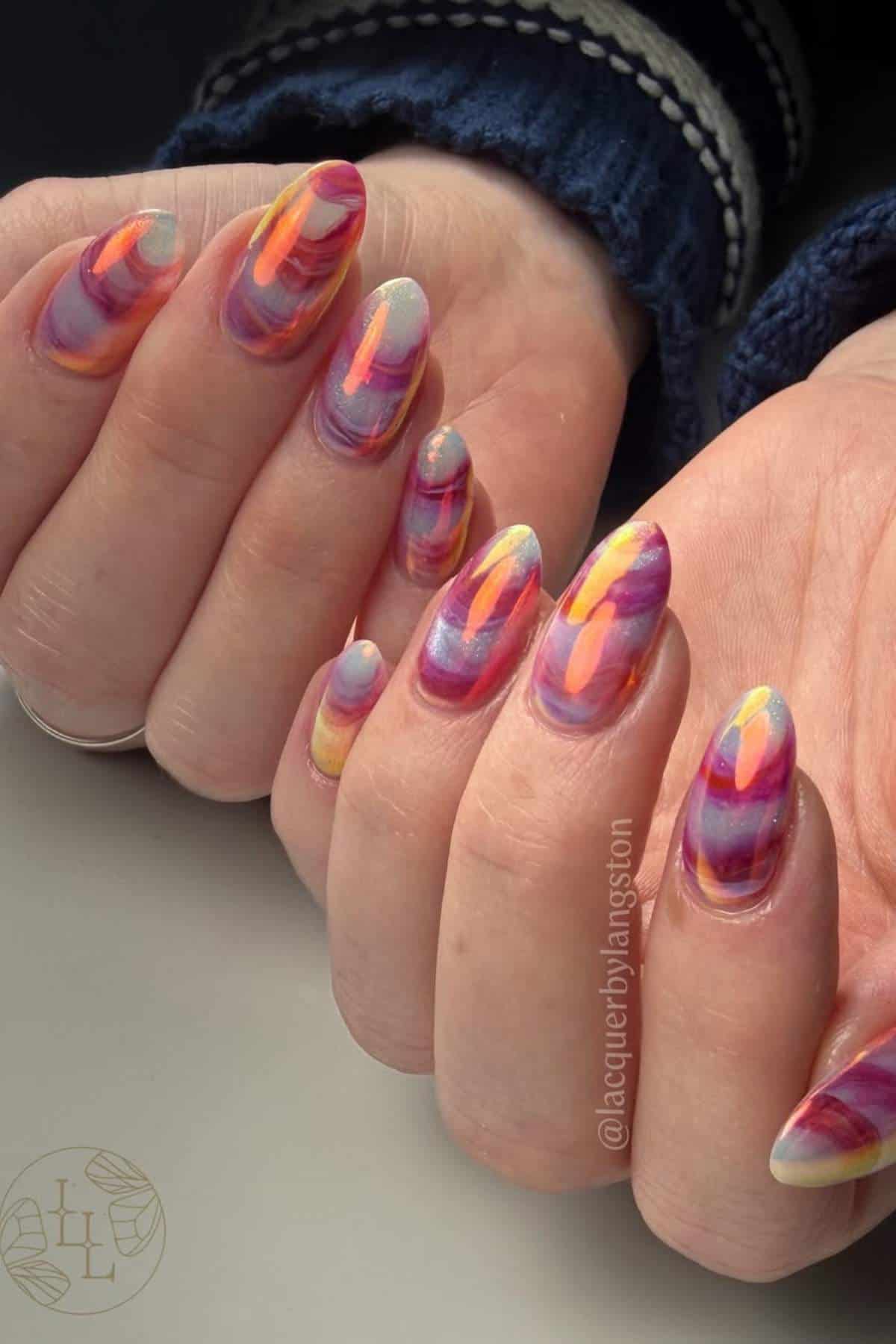 Hands with almond-shaped nails featuring a colorful, abstract marble design in shades of pink, purple, orange, and yellow.