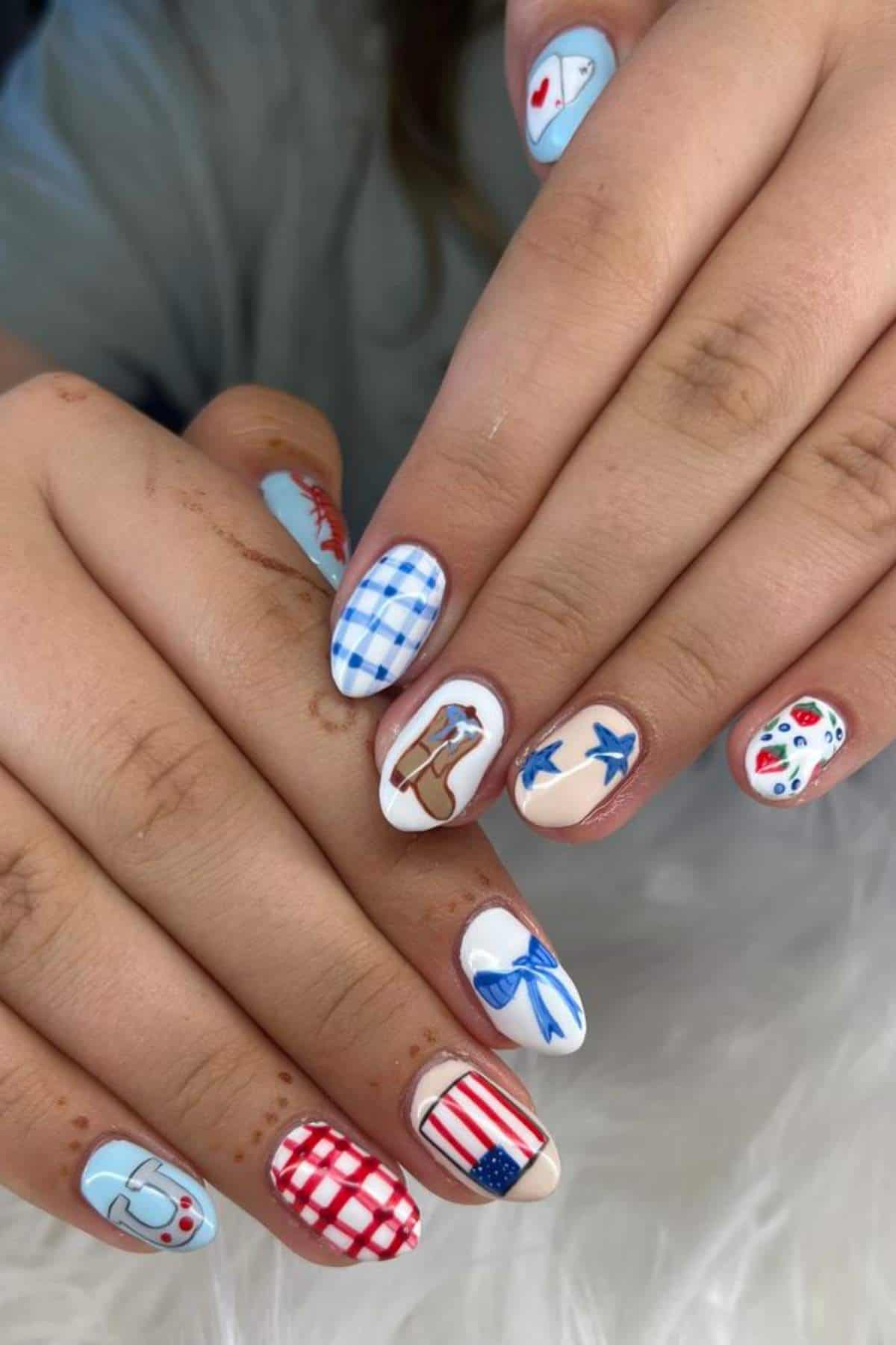 Hands with manicured nails featuring patriotic and picnic-themed nail art, including flags, bows, birds, hearts, and checkered patterns in red, white, blue, and brown tones.