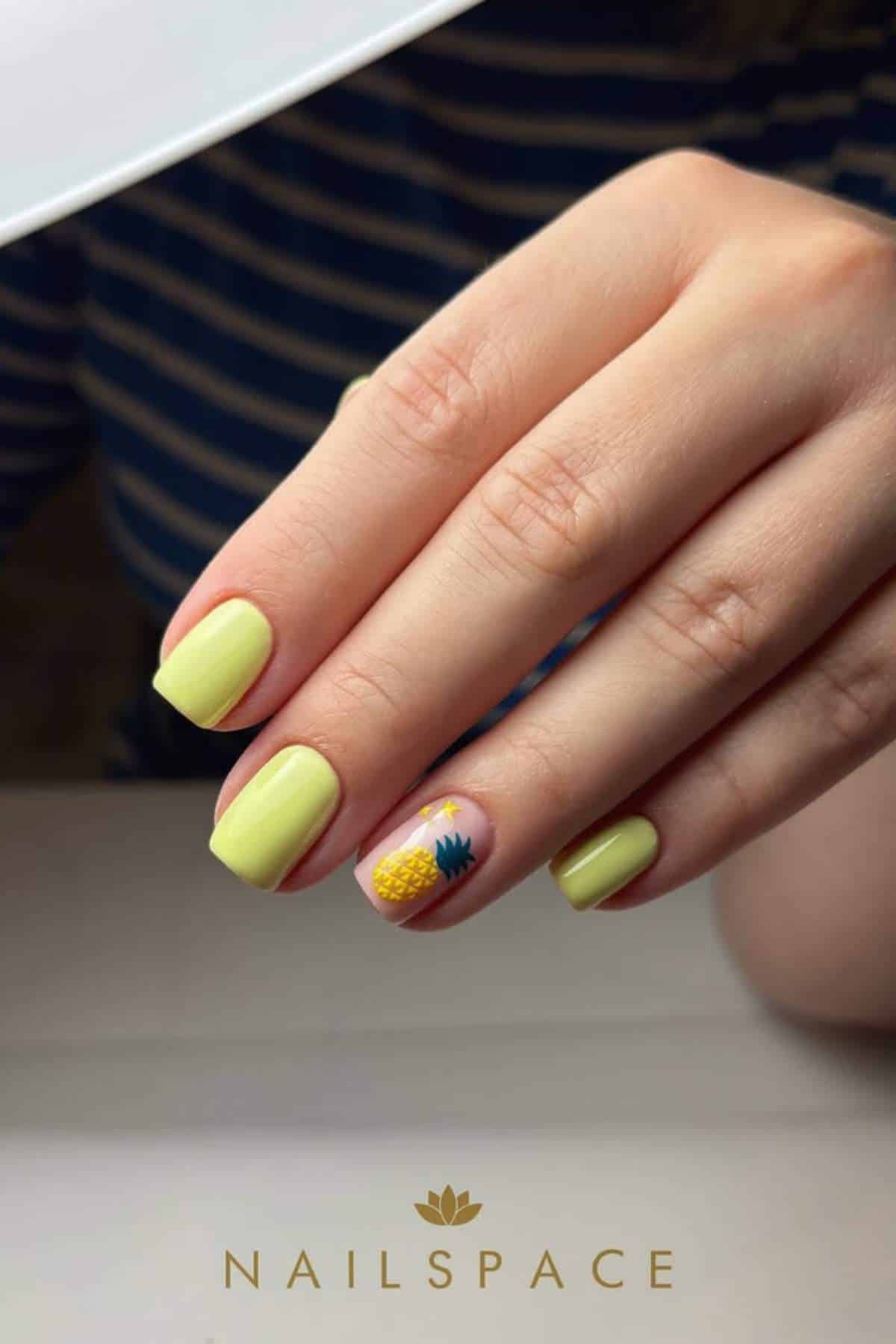 A hand with short yellow-painted nails; the ring fingernail features a small pineapple design. The person is wearing a navy and white striped shirt.