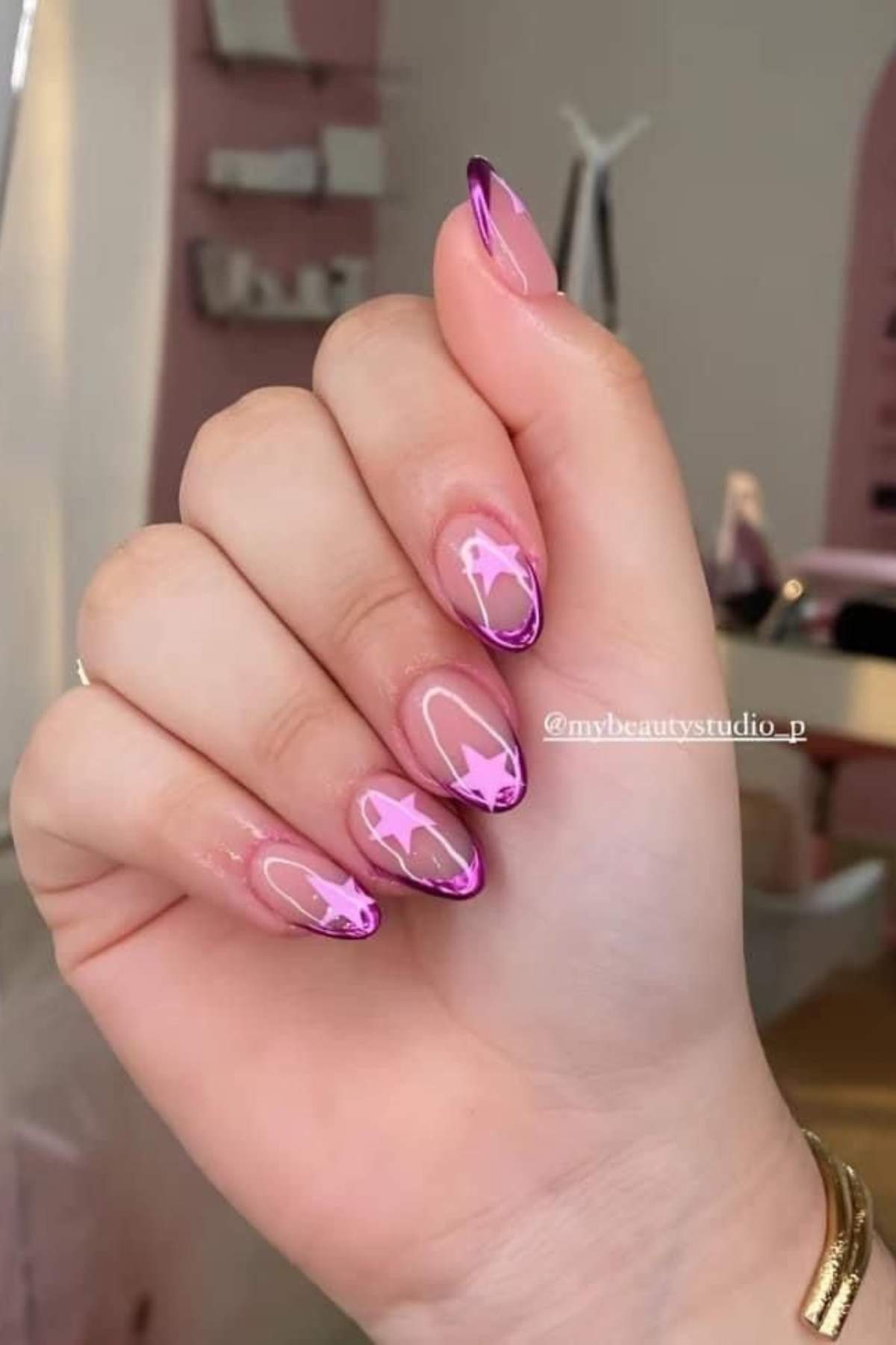 A hand with long, almond-shaped nails featuring pink and purple abstract designs and outlined tips.