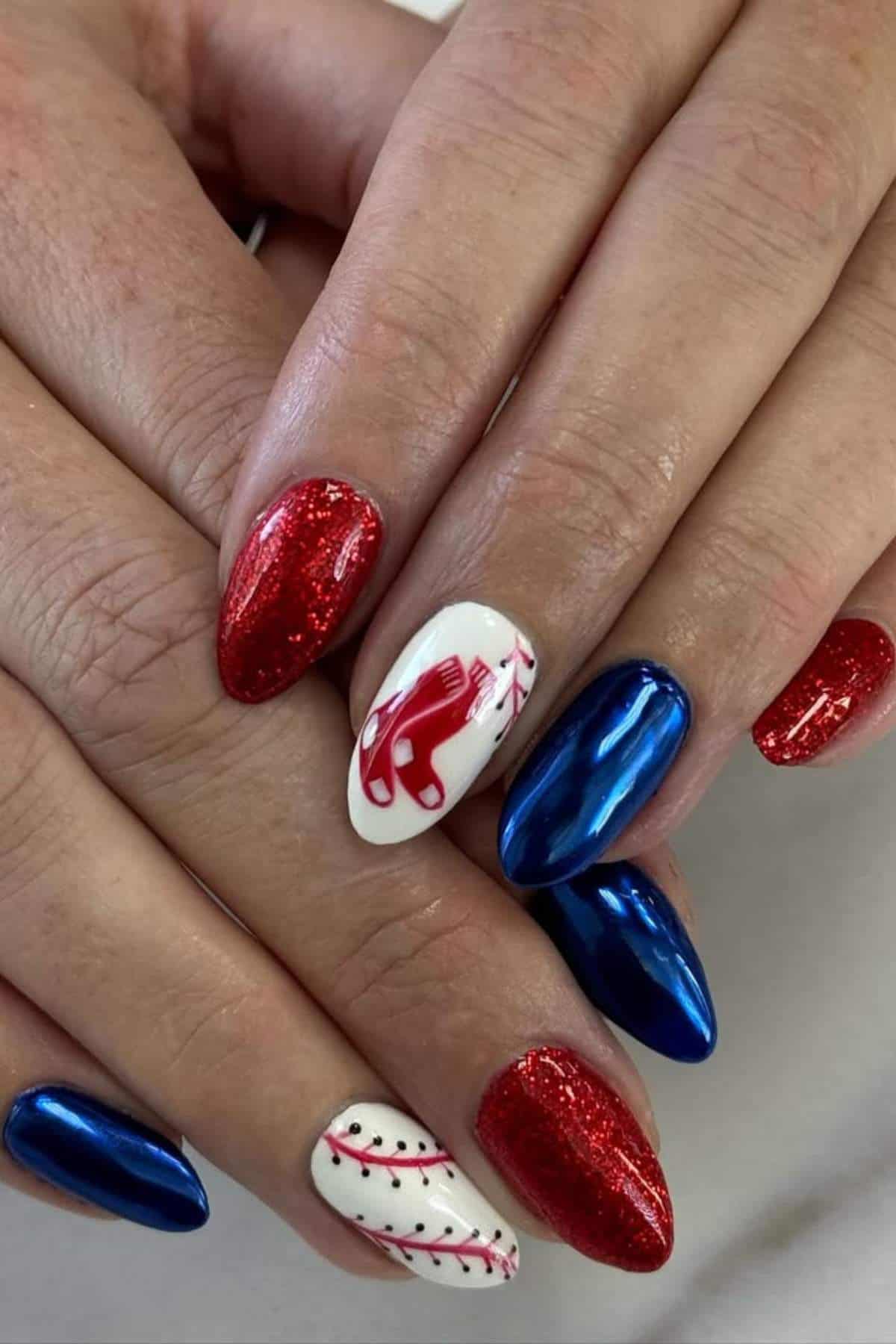 Hands with manicured nails featuring red glitter, metallic blue, and white polish with red ice skate and red stitched line designs.