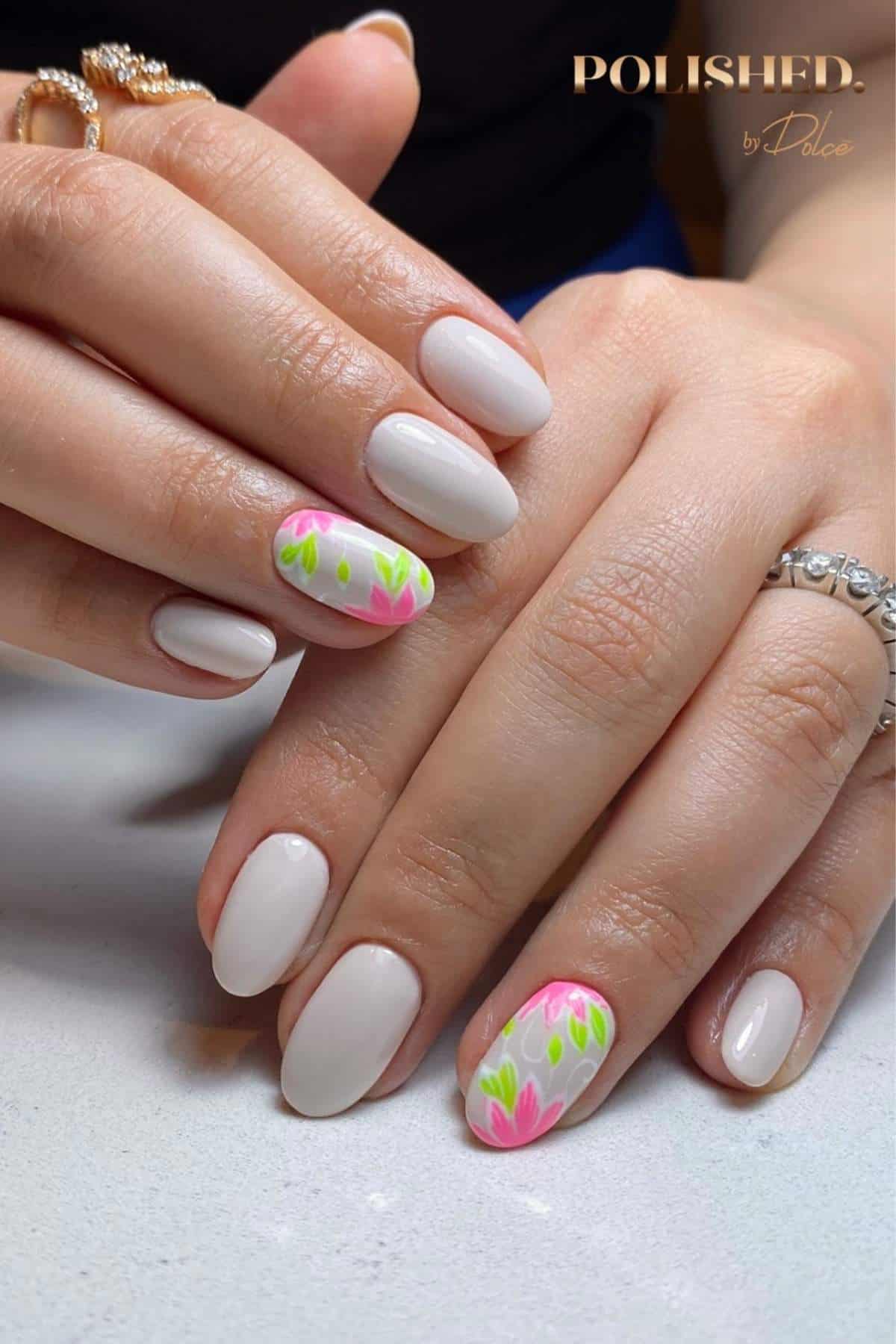 Hands with oval-shaped nails painted light pink; some nails feature pink and green floral designs. Rings are worn on two fingers.