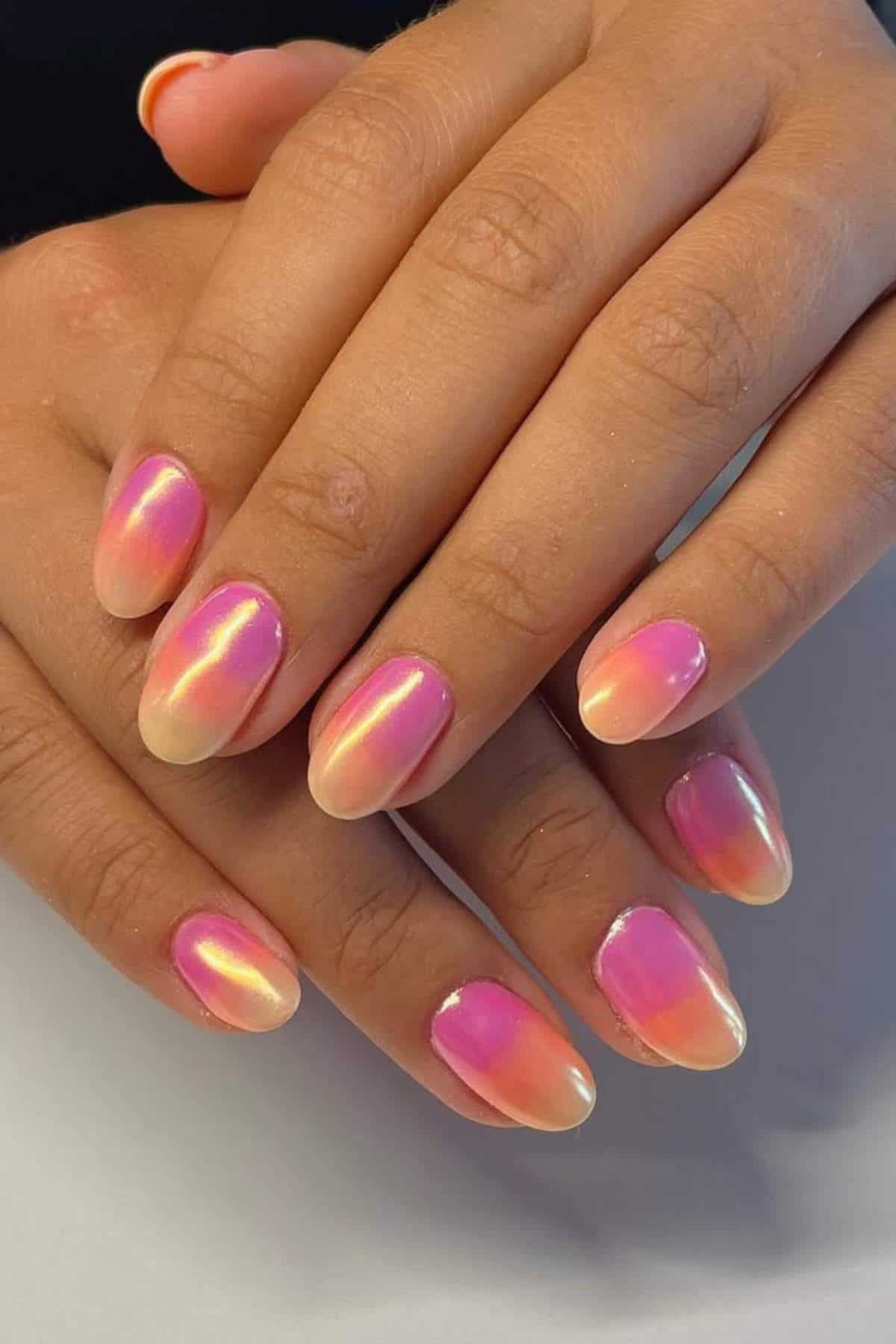 Close-up of hands with almond-shaped nails featuring a pink and peach ombre design with a glossy, iridescent finish.