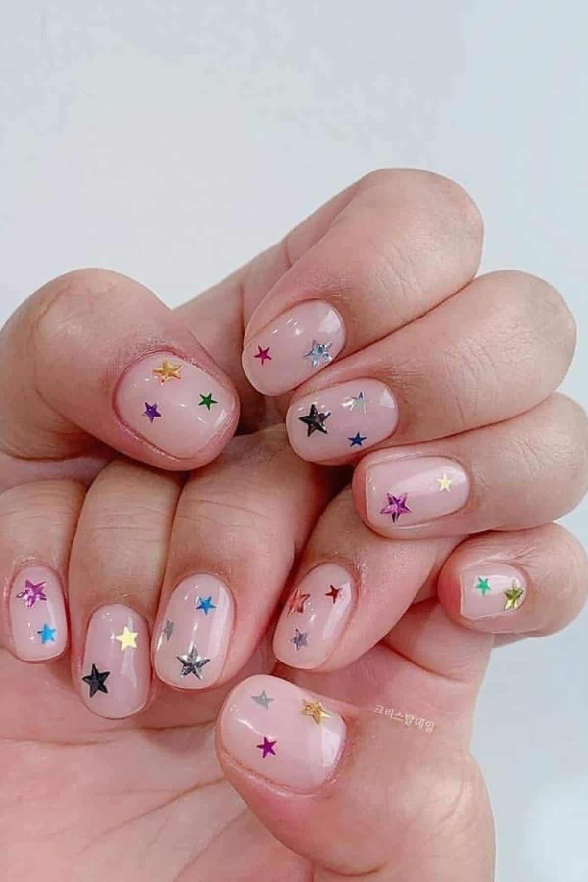 Close-up of hands with short, natural nails painted in a clear polish, decorated with colorful star-shaped stickers.