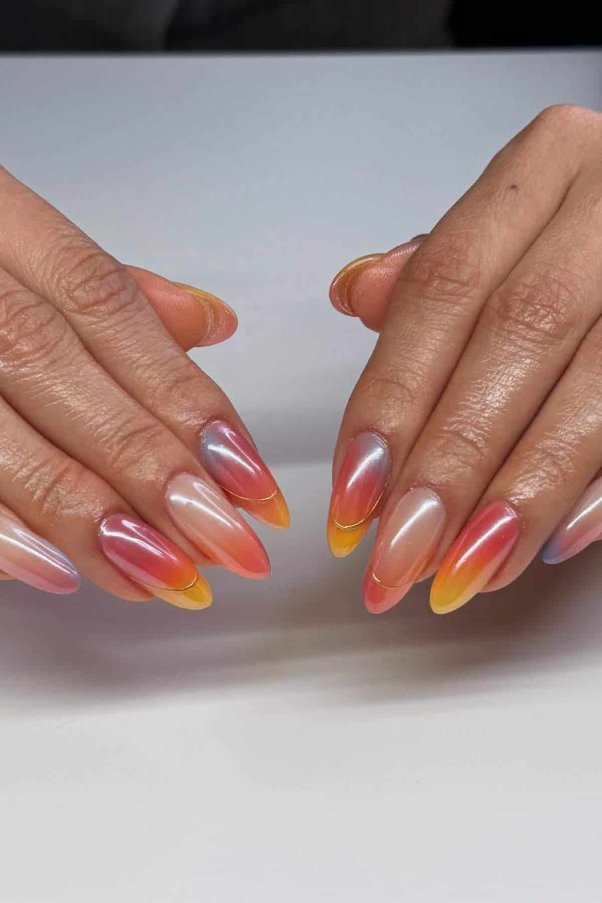 Two hands with almond-shaped nails featuring a gradient design in shades of pink, orange, yellow, and subtle blue tips.