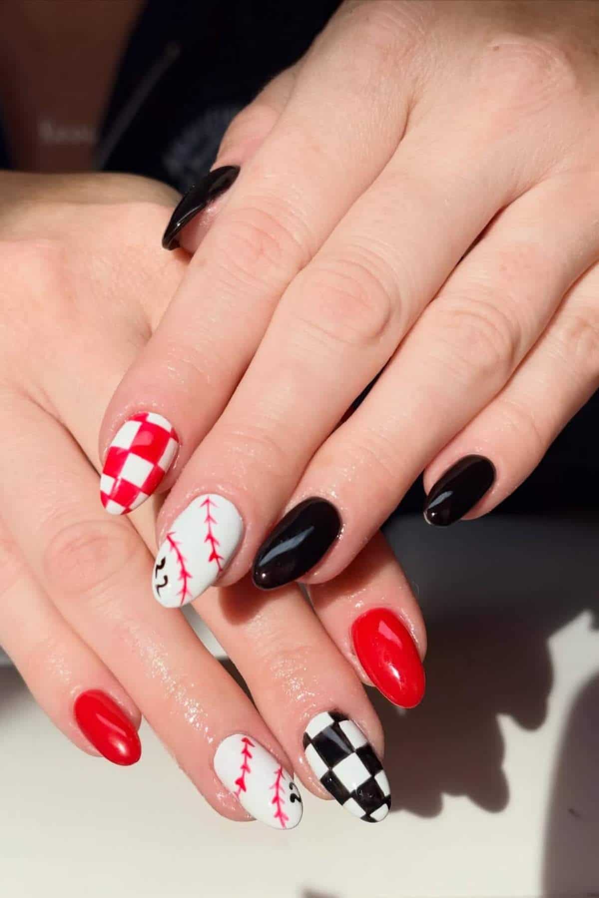 Hands with manicured nails featuring black, red, and white polish, with designs including checkerboard, baseball stitching, solid colors, and geometric patterns.