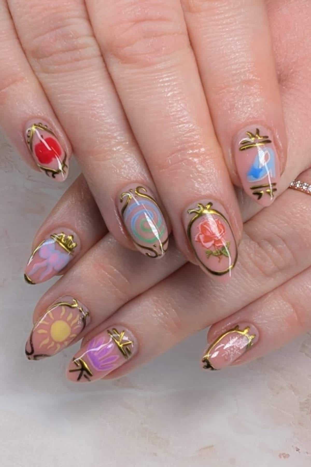 Close-up of hands with long almond-shaped nails, each featuring colorful, abstract designs and outlined in metallic gold. Designs include flowers, sun, heart, swirl, and pastel patterns.