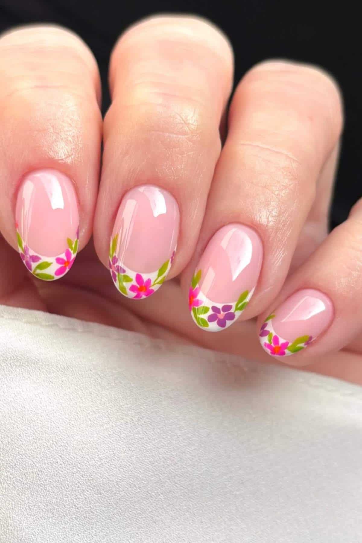 A hand with light pink nails featuring small, colorful floral designs with green leaves near the tips.