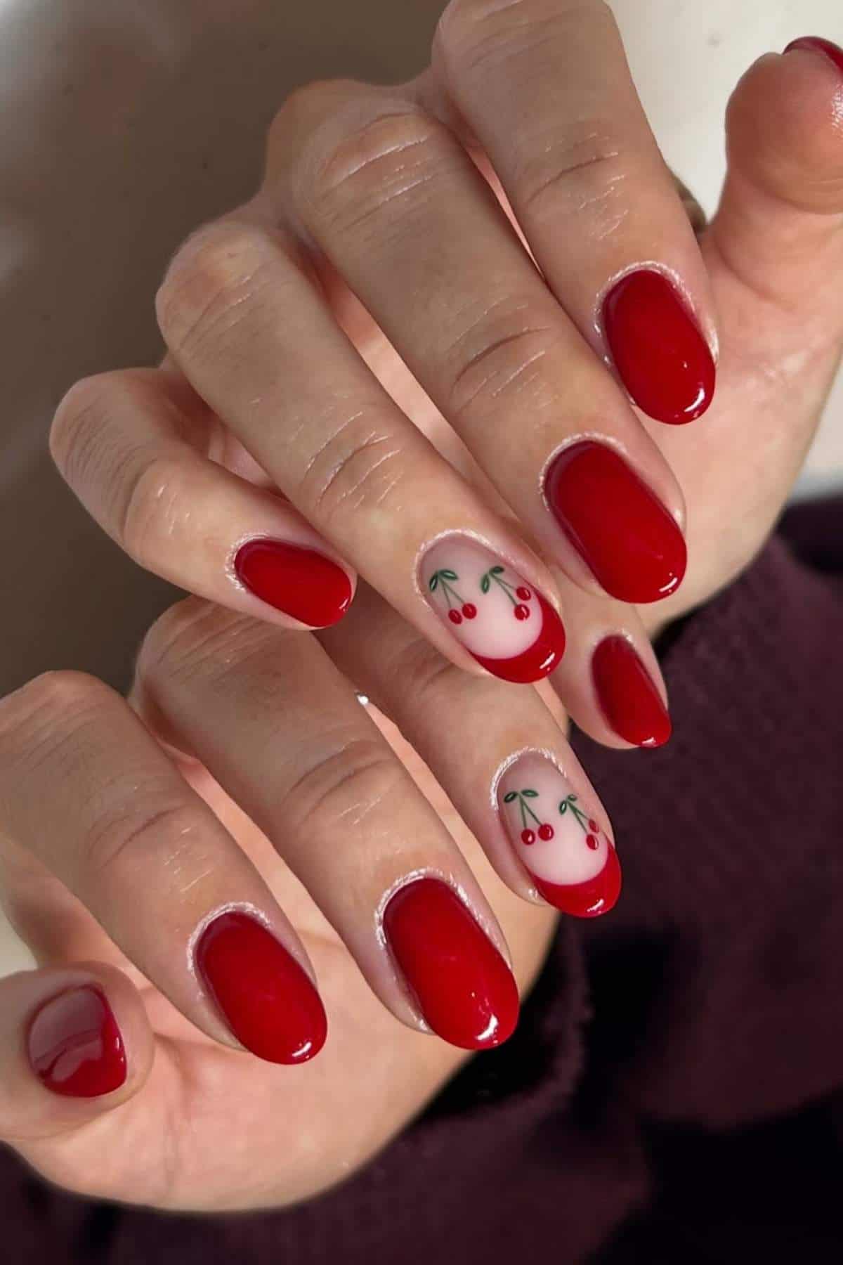 Hands with red nail polish; two accent nails feature small red cherry designs on a nude background.