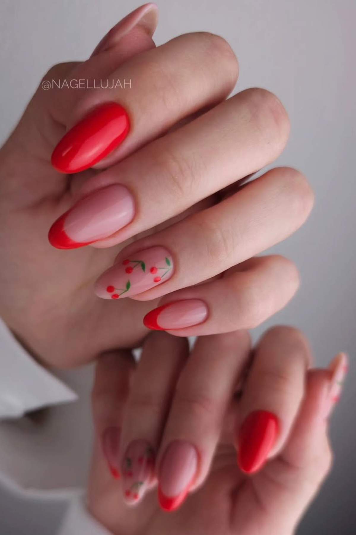 A hand with almond-shaped nails features a red French tip manicure and two accent nails with small red and green floral designs.