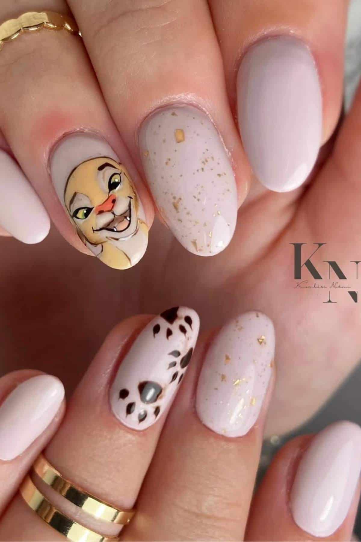 Close-up of manicured nails with pale pink polish, gold flecks, a cartoon lion character, and a paw print design accent nail.