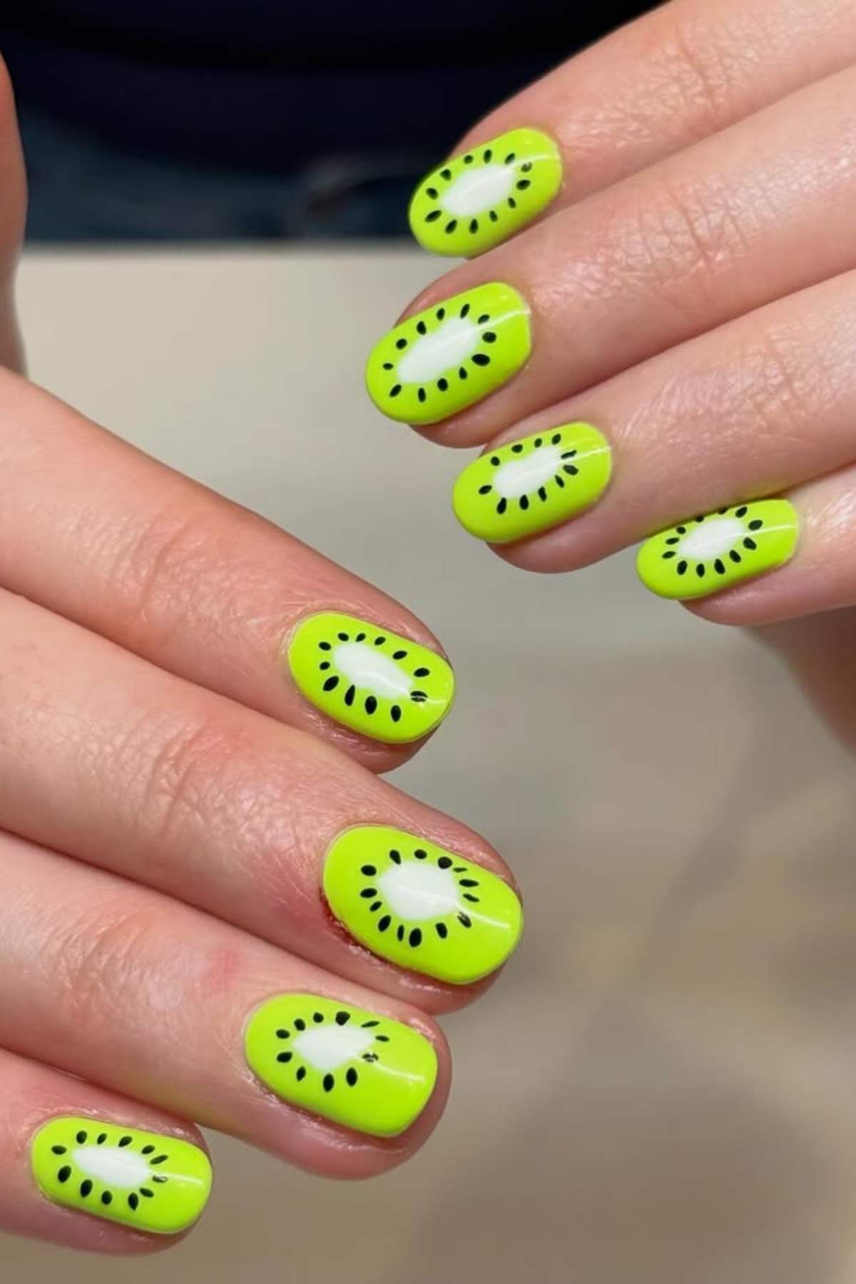 Close-up of hands with fingernails painted bright green and decorated with black and white designs resembling kiwi fruit slices.