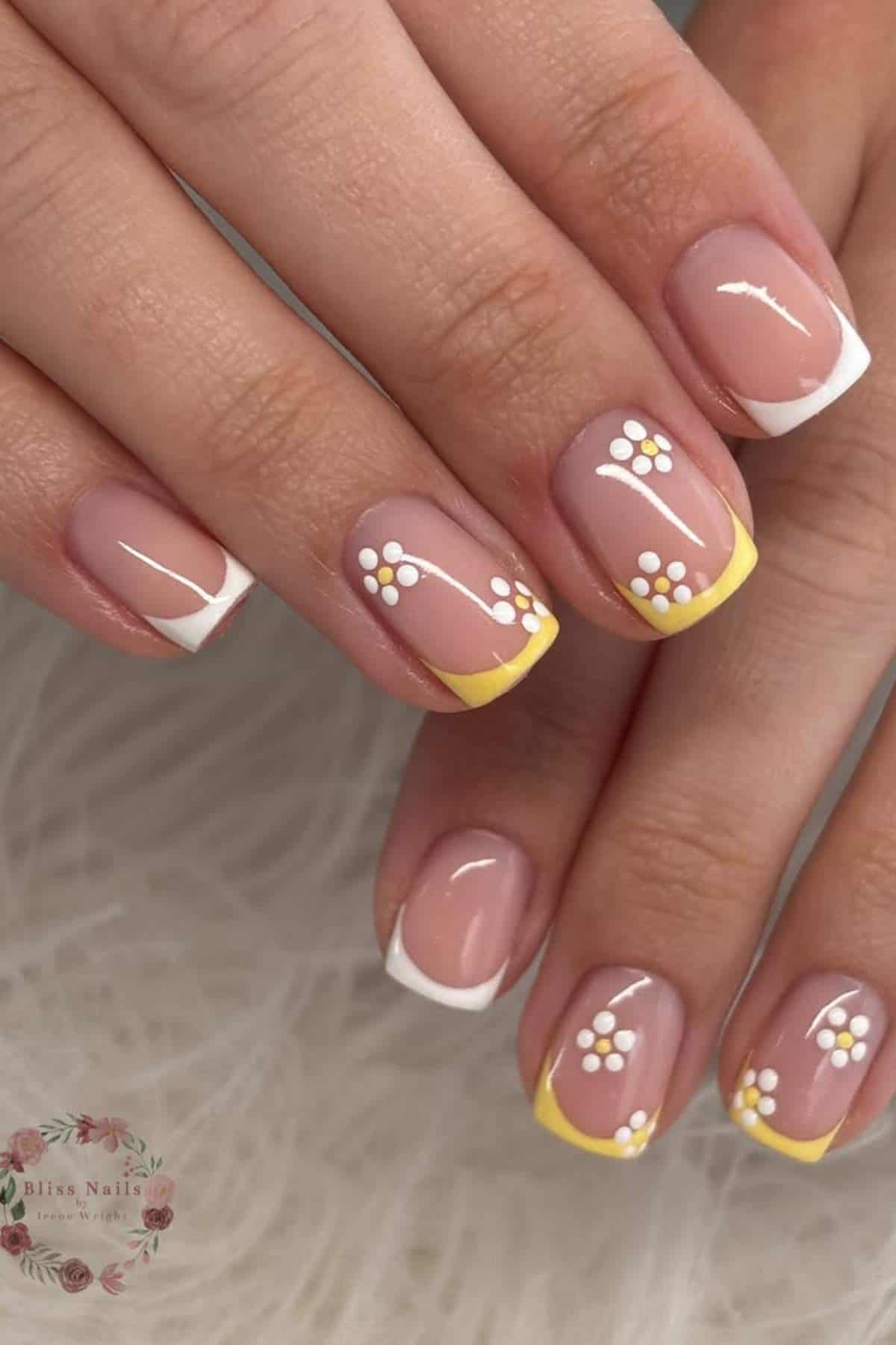 Close-up of hands with square-shaped nails featuring a French manicure in white and yellow, accented with small white and yellow flower designs.
