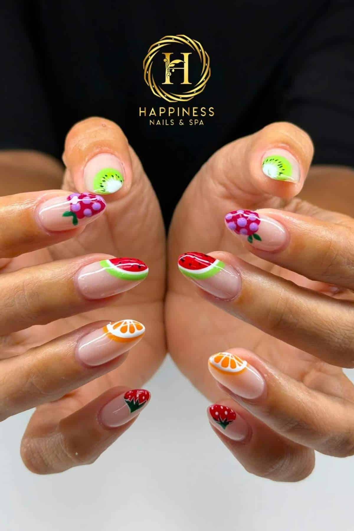 Close-up of hands with manicured nails featuring colorful fruit designs, including kiwi, grapes, oranges, and strawberries, with a "Happiness Nails & Spa" logo in the background.