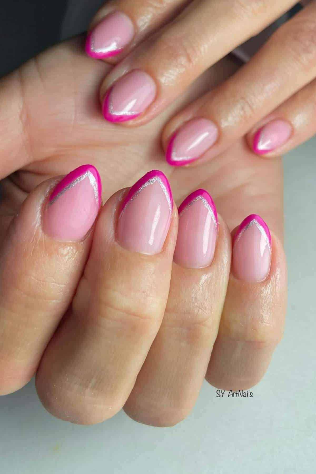 Close-up of hands with almond-shaped nails featuring a light pink base, bright pink French tips, and a thin silver line along the tips.