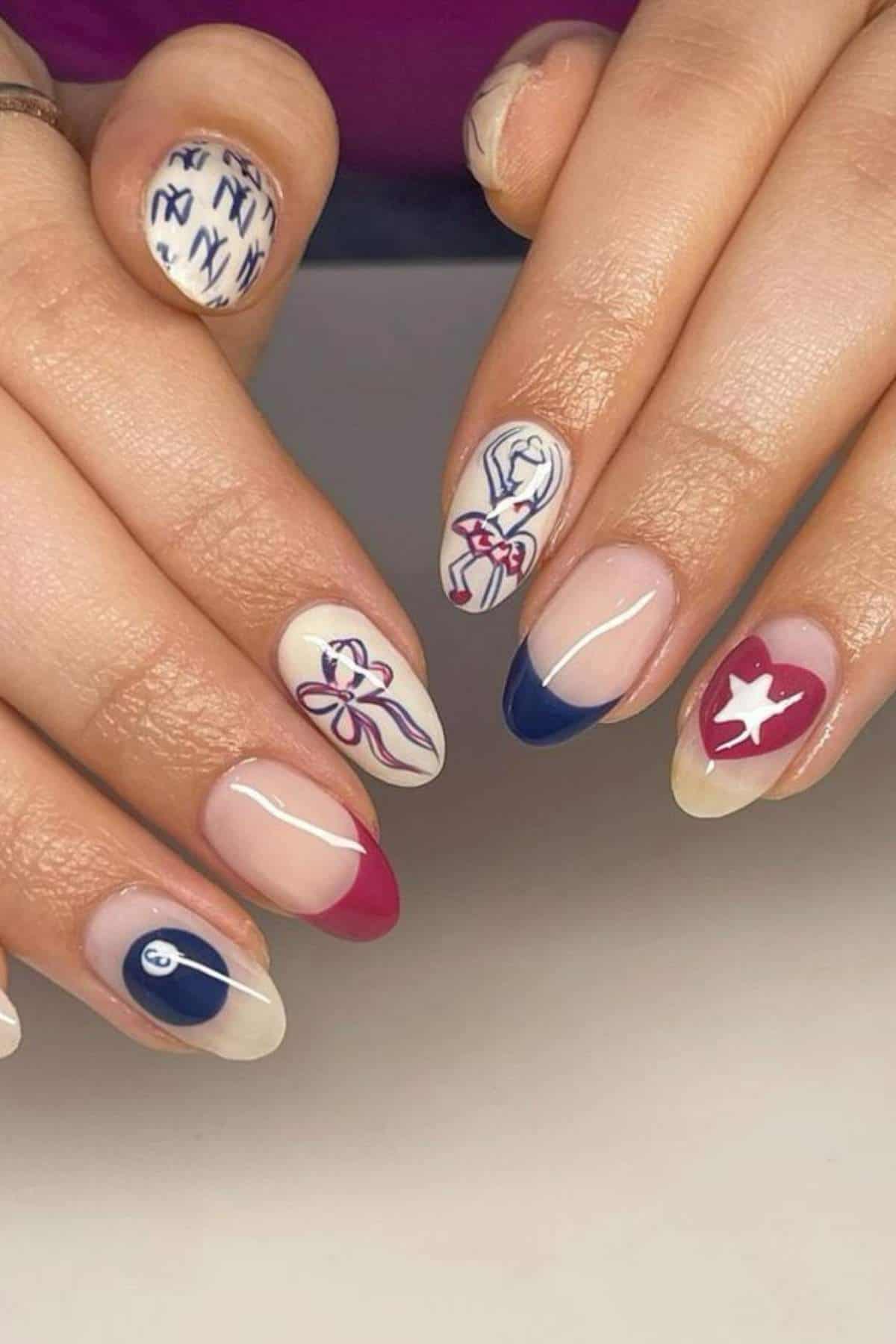 A hand with long almond-shaped nails featuring red, blue, and white nail art designs, including bows, stripes, a star, and abstract patterns.