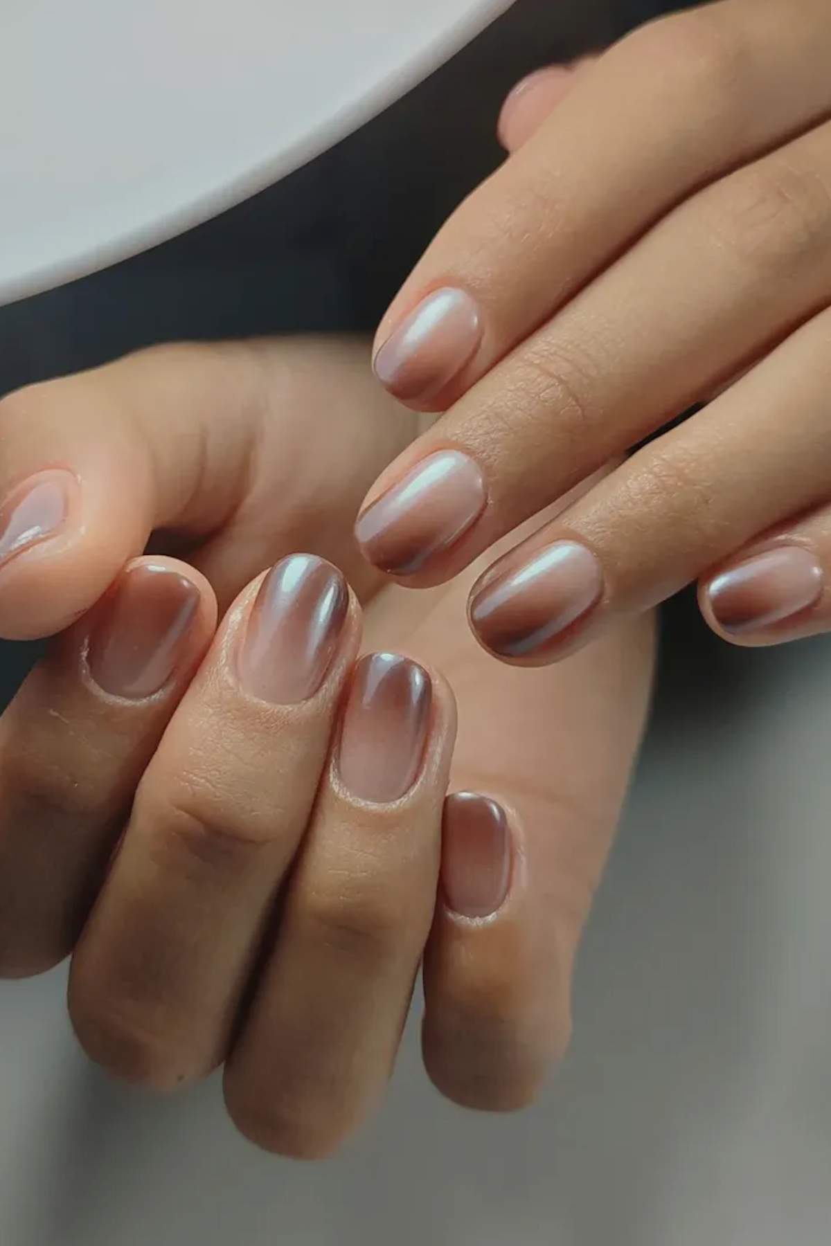 Close-up of hands with short, neatly manicured nails painted in a pearlescent nude polish.