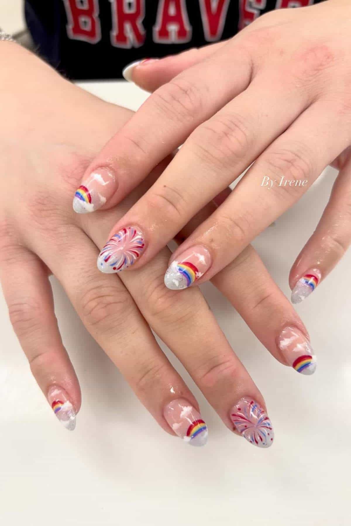 Almond-shaped nails with a clear coat, white tips, and designs of rainbows, fireworks, and clouds.