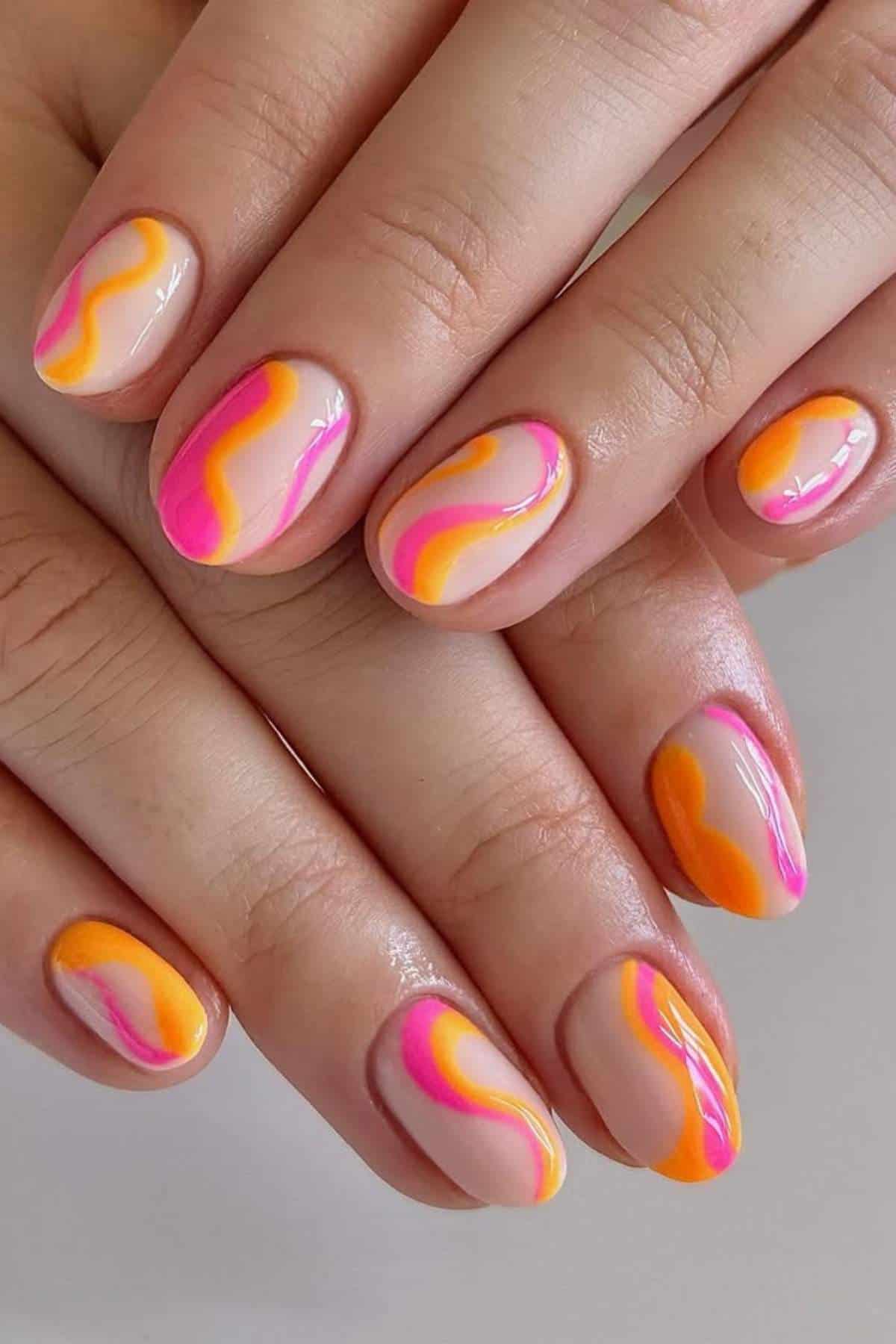 Close-up of hands with nude manicure featuring pink, orange, and yellow wavy abstract designs on short, oval-shaped nails.