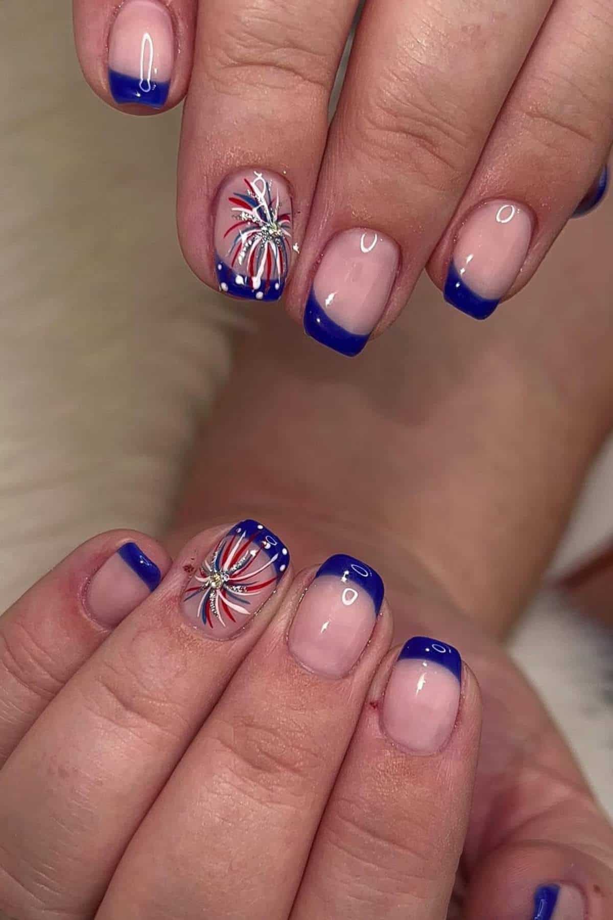 French tip nails with blue polish, and two accent nails featuring a red, white, and blue firework design with glitter.