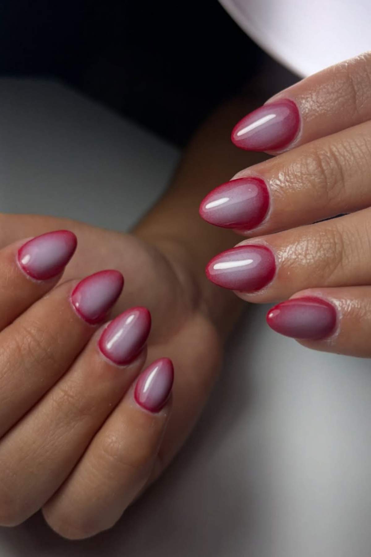 Hands with almond-shaped nails featuring a gradient pink manicure with darker pink tips, shown against a neutral background.