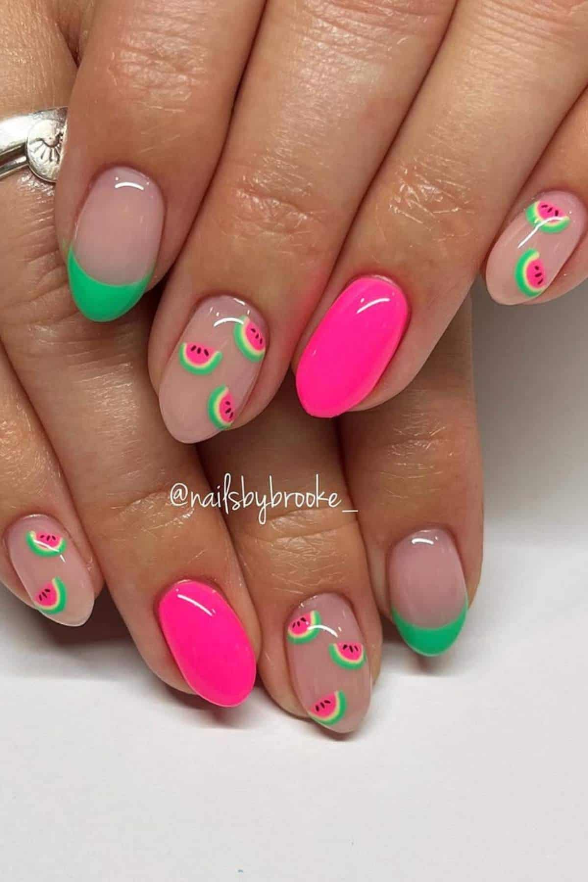 Hands with manicured nails featuring a mix of neon pink, green French tips, and small watermelon slice designs on a natural base.