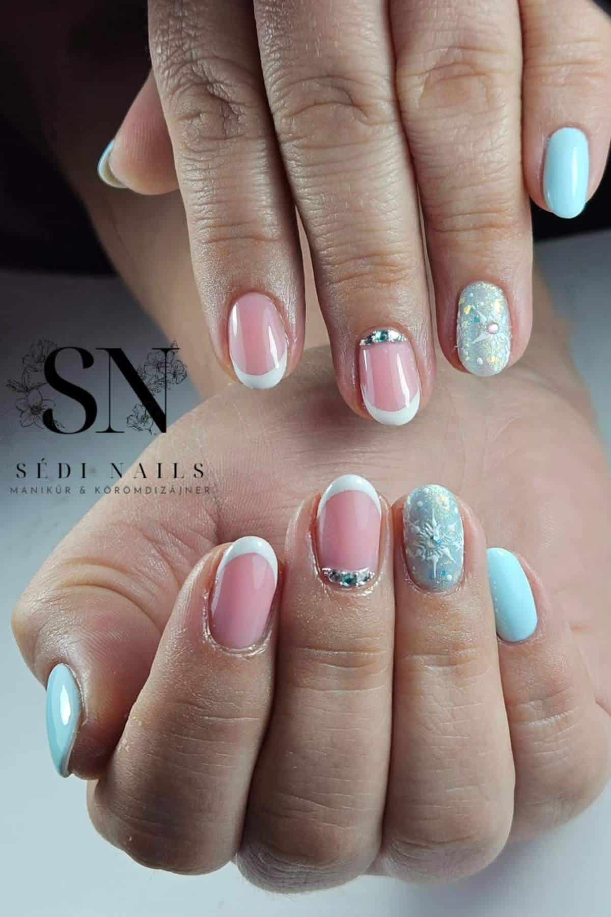 Hands with manicured nails featuring French tips, light blue polish, silver rhinestone accents, and a glittery white design on ring fingers.