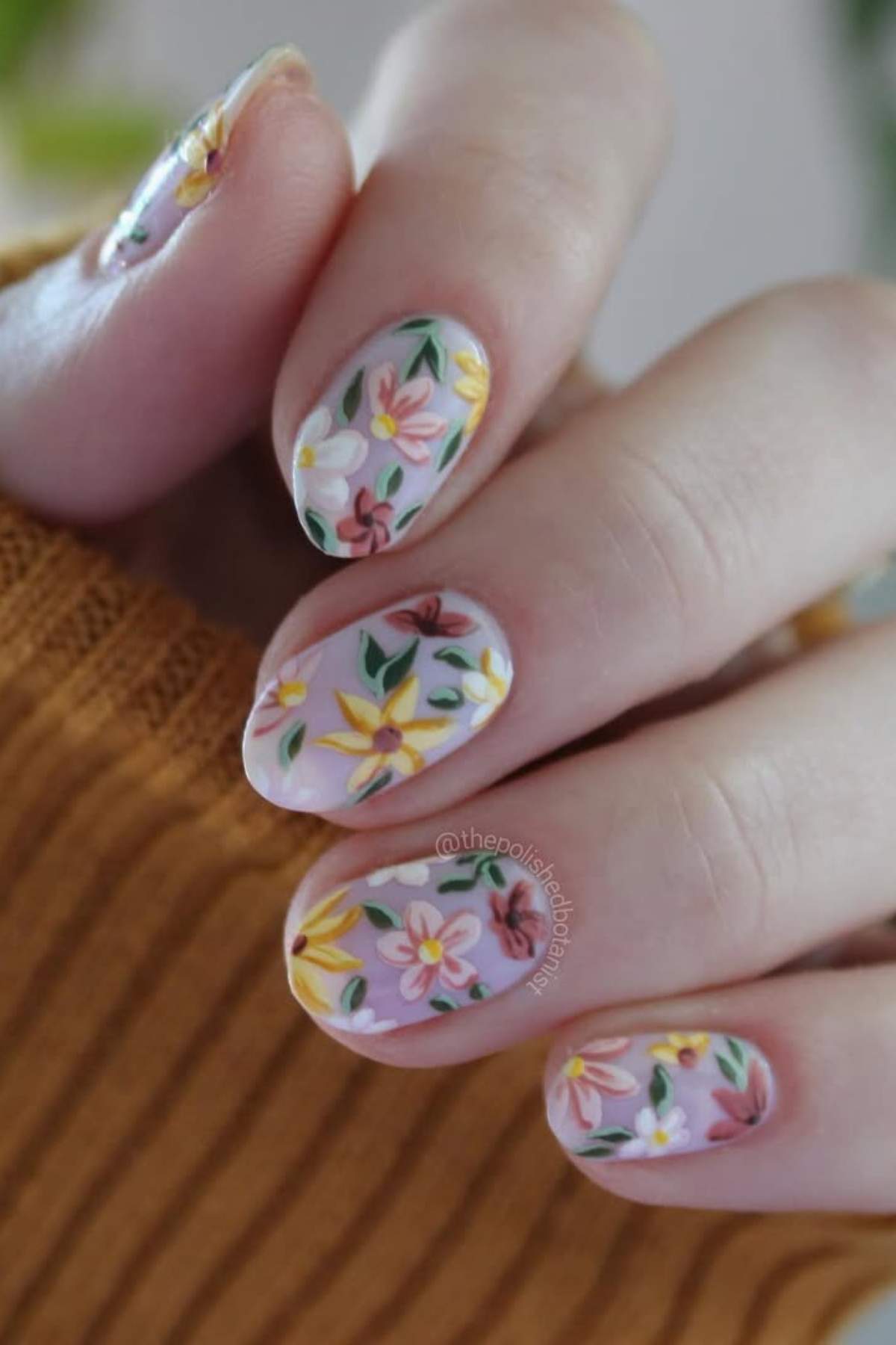 A hand with almond-shaped nails painted with a light pink base and decorated with colorful floral designs.