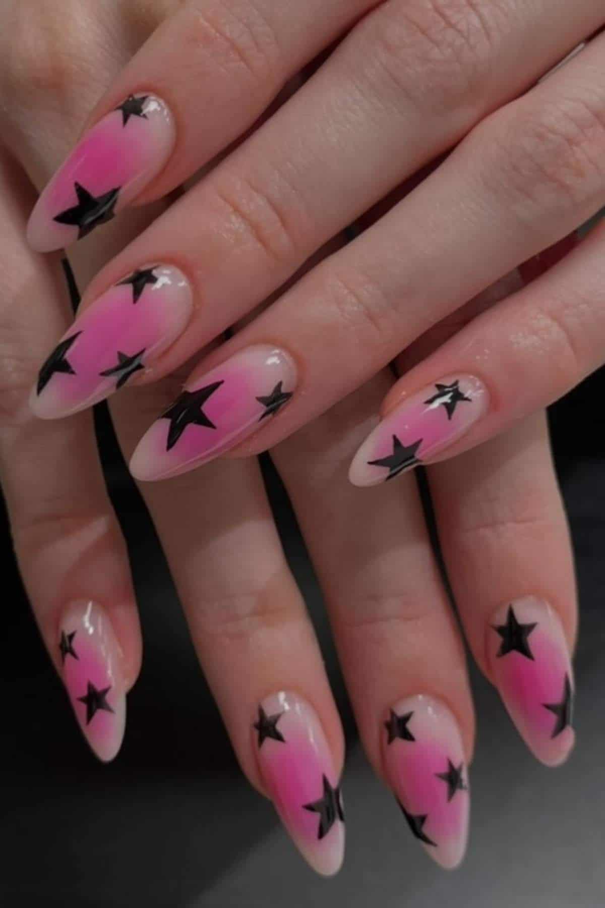 Hands with long almond-shaped nails painted pink with black star designs.